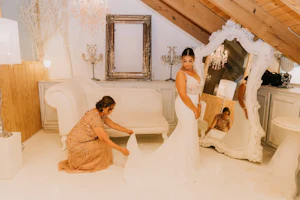 Mother of bride straightening the bride's train in beautiful ivory and gold room.