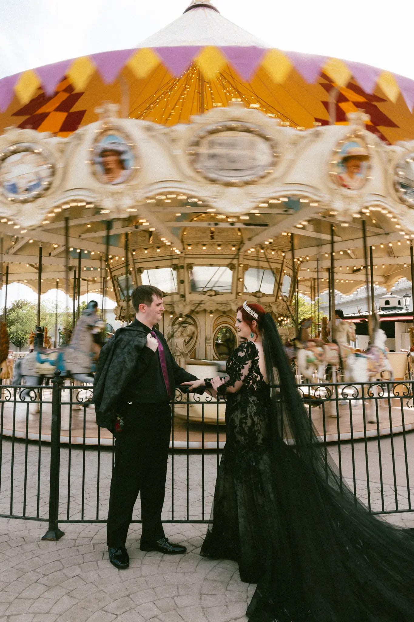 Bride Wearing Black Lace Wedding Dress Called Zander Lane By Sottero And Midgley With Groom Standing In Front Of A Moving Carousel