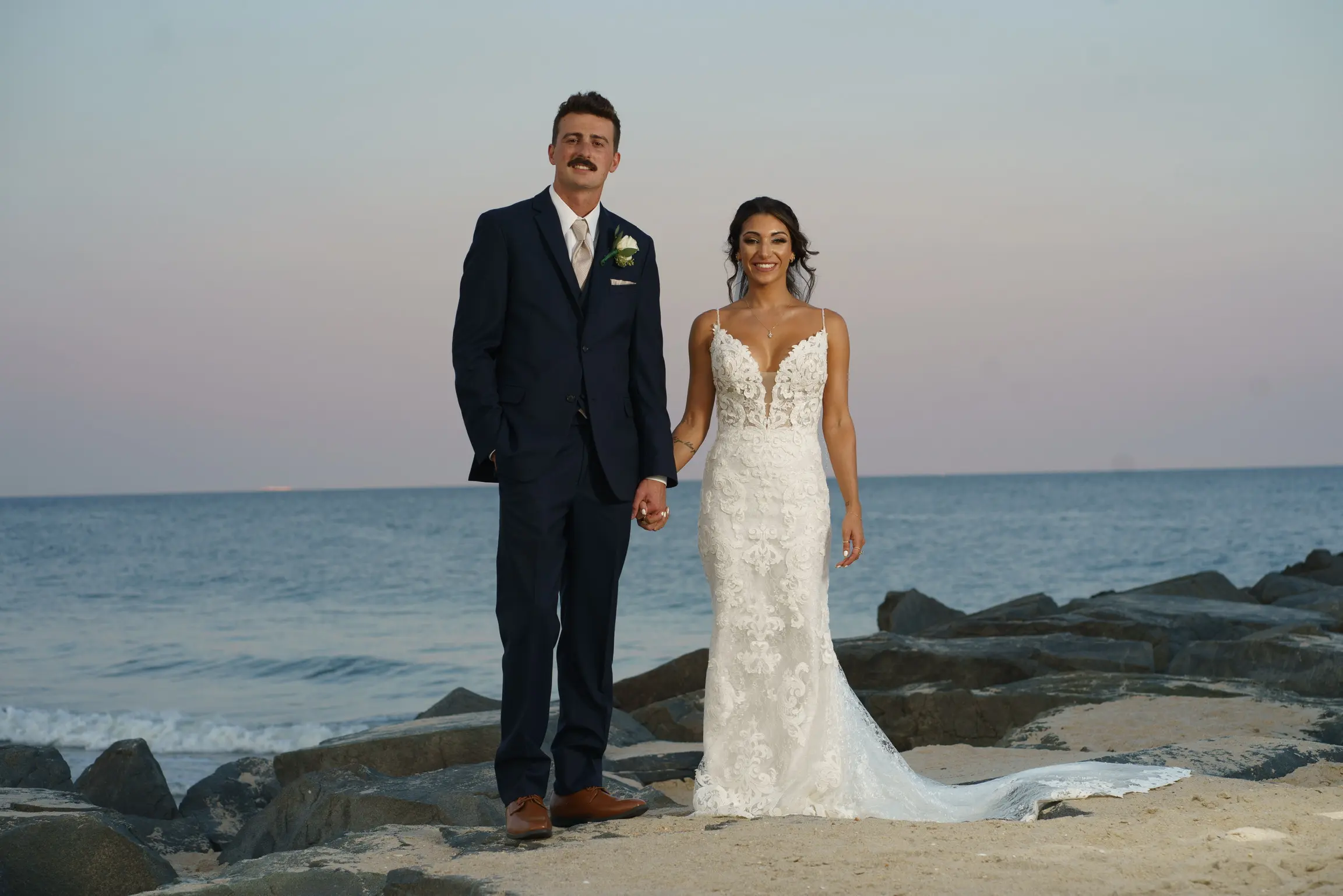 Groom Holding Hands with Bride in Front of Ocean Wearing Mermaid Wedding Dress called Tuscany by Maggie Sottero.