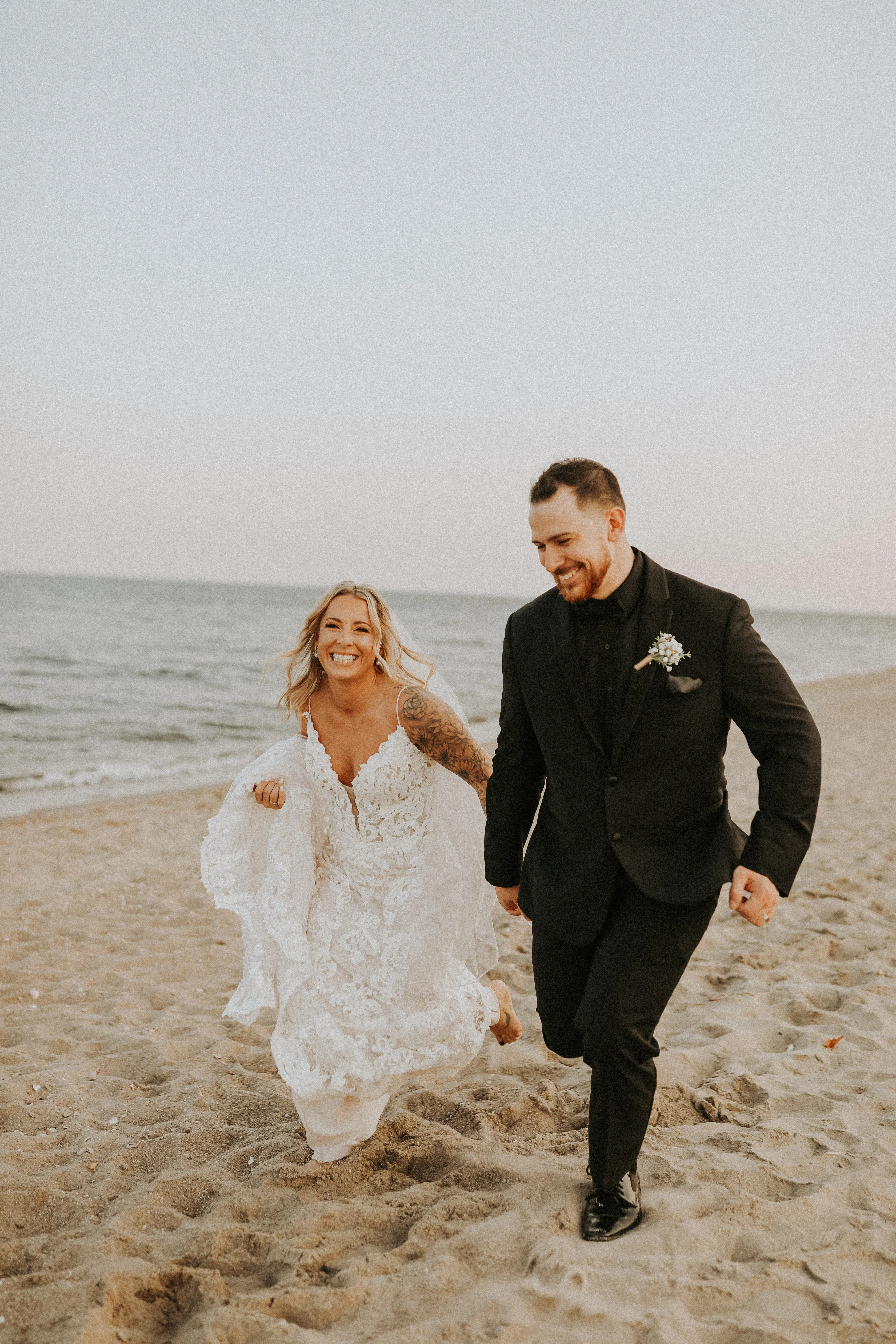 Bride In Lace Sheath Wedding Gown Name Tuscany Lynette By Maggie Sottero Bride And Groom Running On Beach