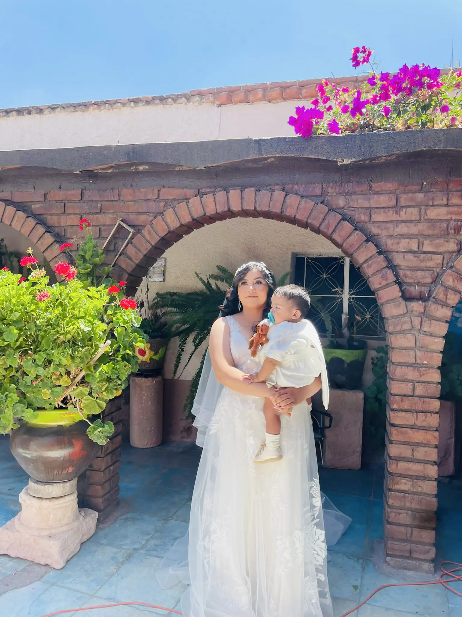 Bride Holding Baby Wearing Romantic A-line Wedding Dress Called Priscilla by Rebecca Ingram.