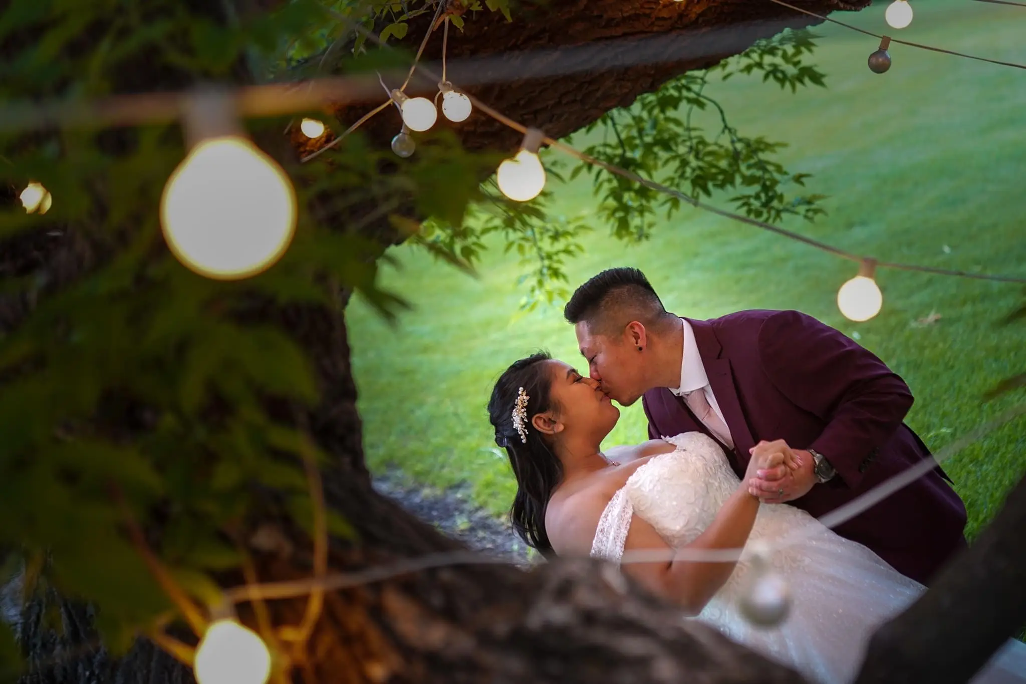 Bride and groom kissing under a tree with pretty lights.
