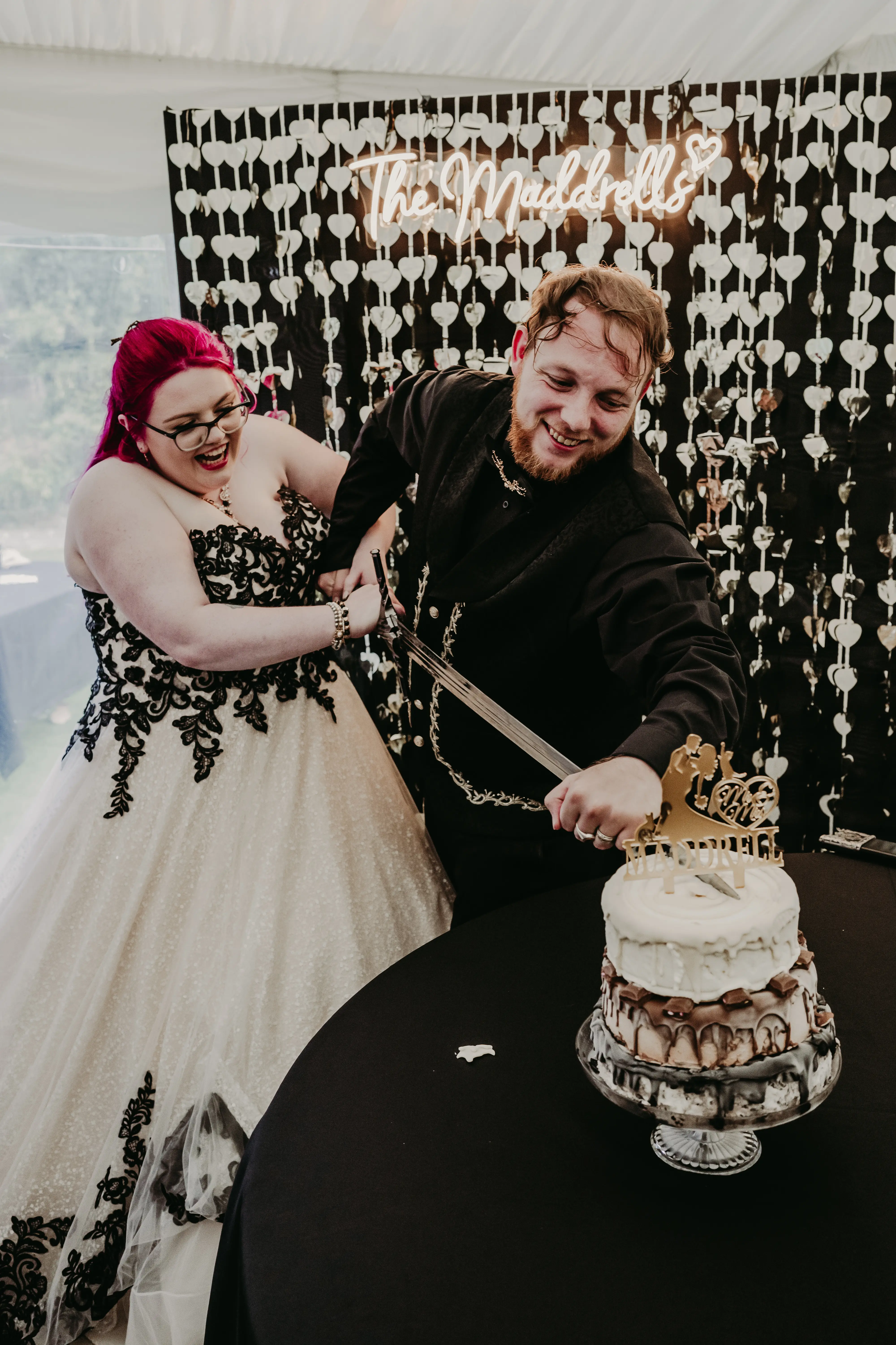 Bride Wearing Gothic Black Lace Wedding Dress Called Tristyn By Maggie Sottero With Groom Cutting The Cake With A Sword