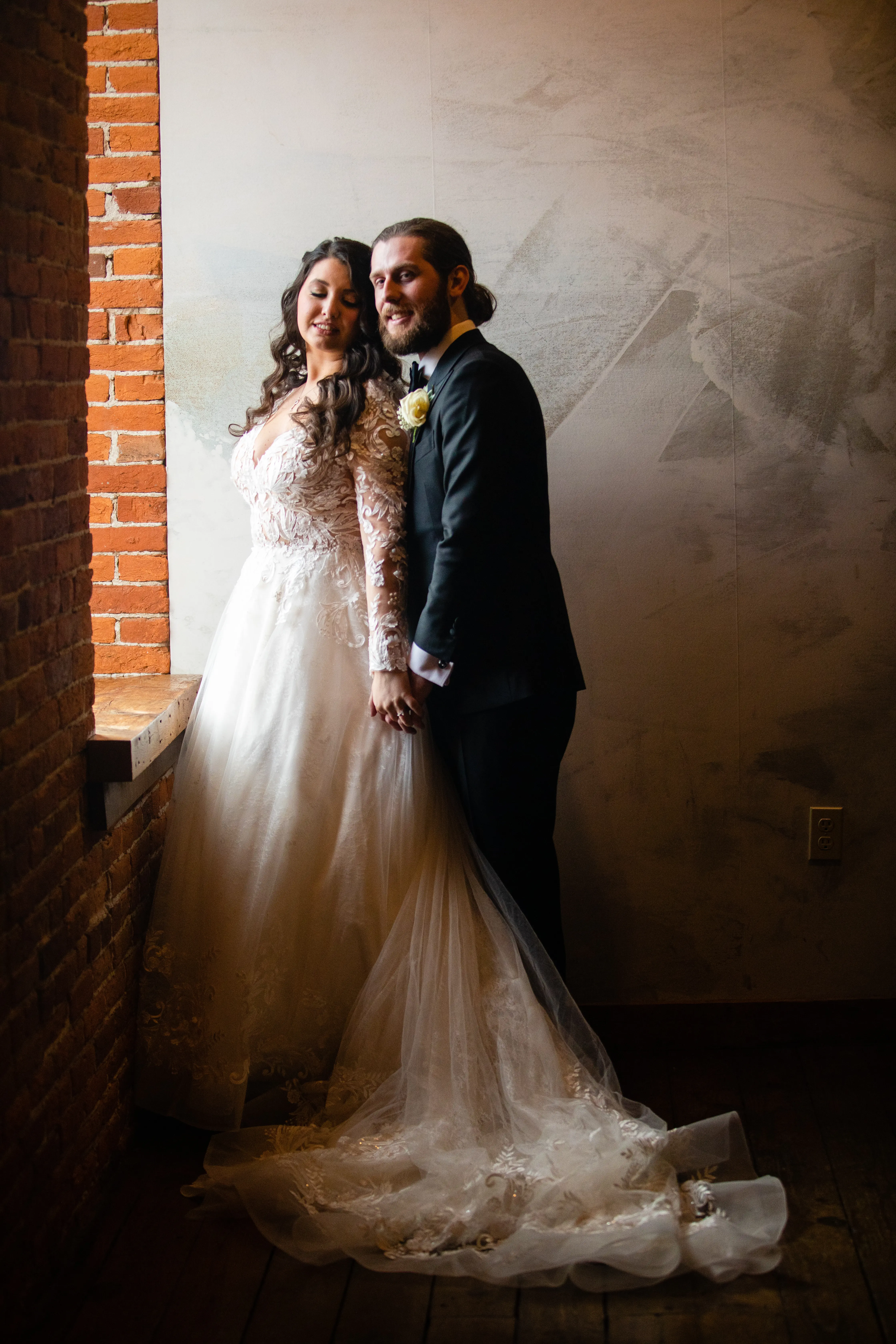 Bride And Groom Standing Together. Bride Wearing Lace Long Sleeve Wedding Dress Called Zander By Sottero And Midgley