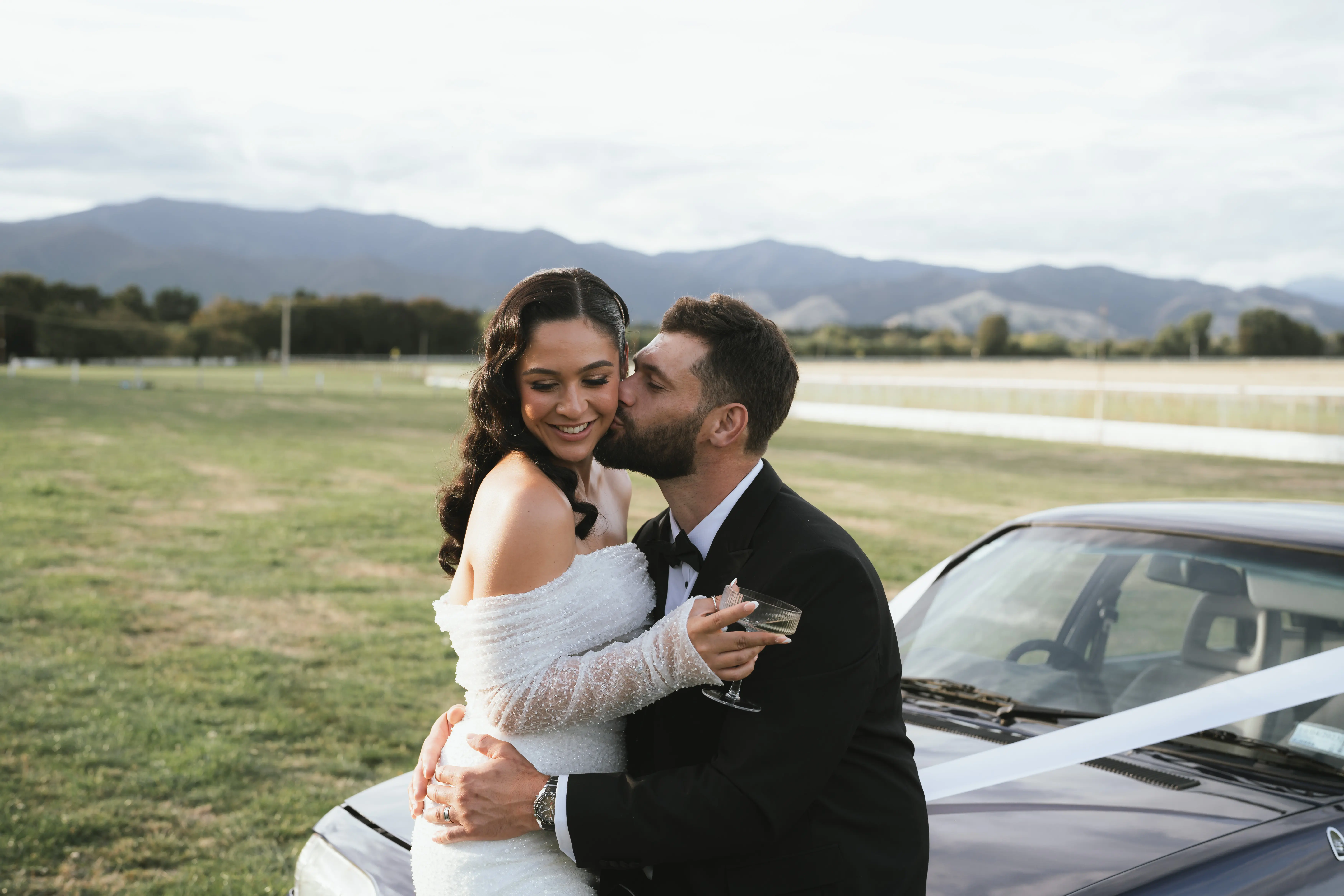Bride wearing Drew by Maggie Sottero and her husband on a car
