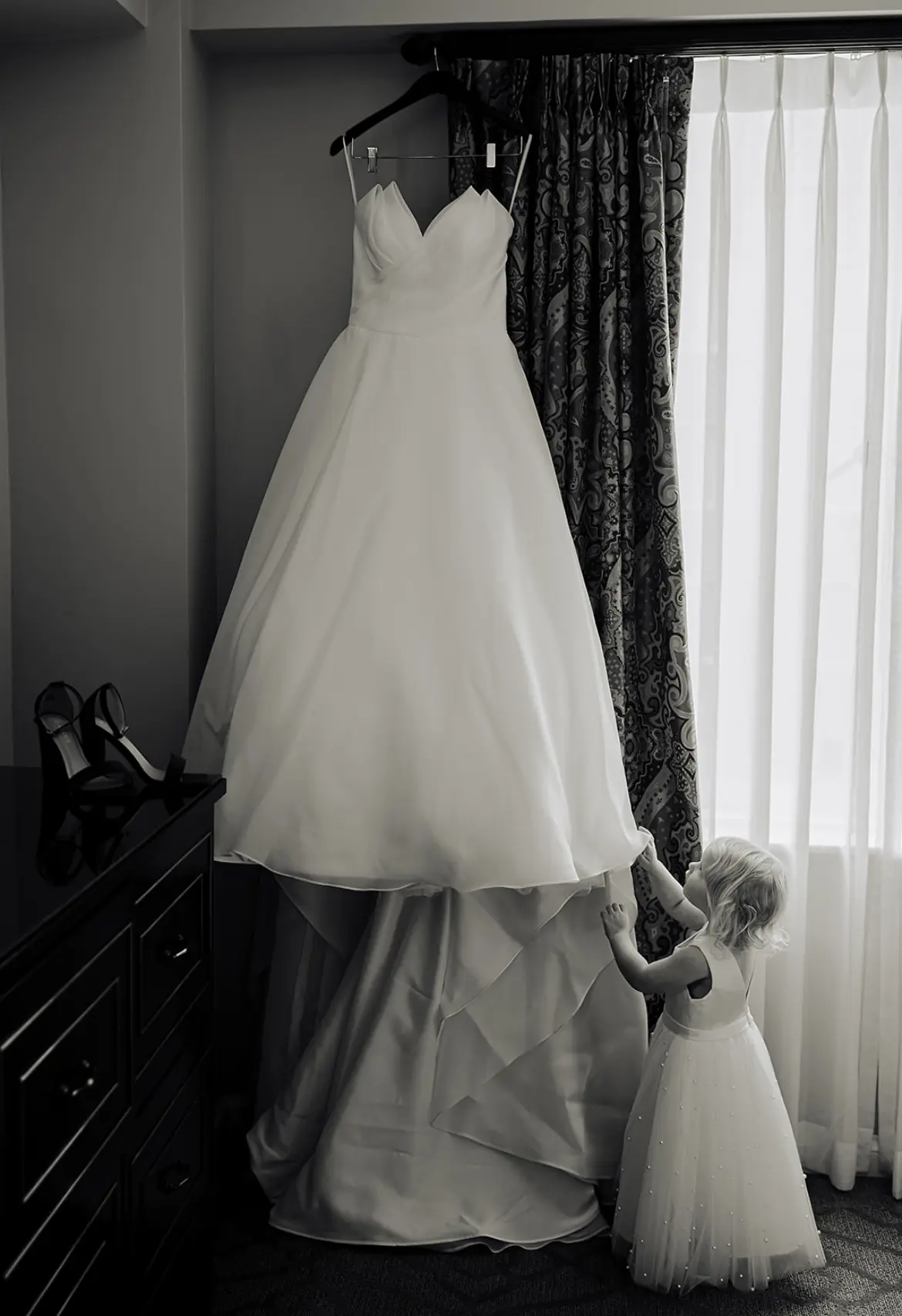 Modern Princess Wedding Dress Called Aubrielle By Maggie Sottero Handing From Window With Flower Girl Admiring It