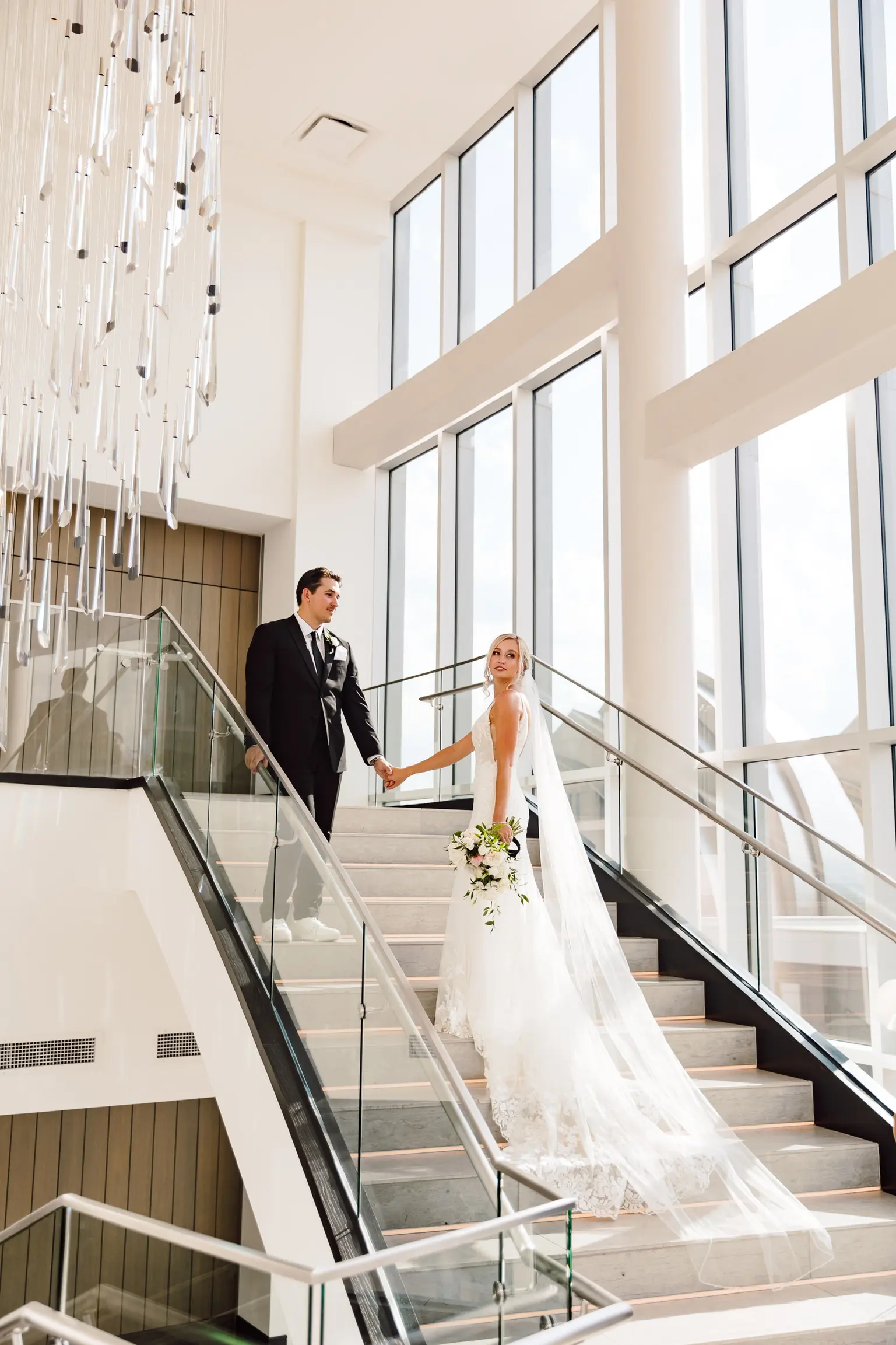 Bride Wearing Sparkle Lace Long Train Wedding Dress Called Fontaine By Maggie Sottero With Groom Under Glass Chandelier