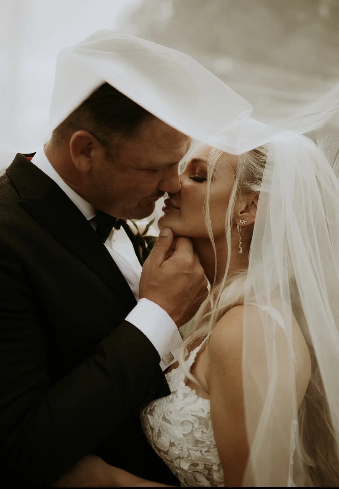 Bride wearing Lace Fit-and-Flare Wedding Dress called Tuscany Lynette by Maggie Sottero kissing the groom under her veil