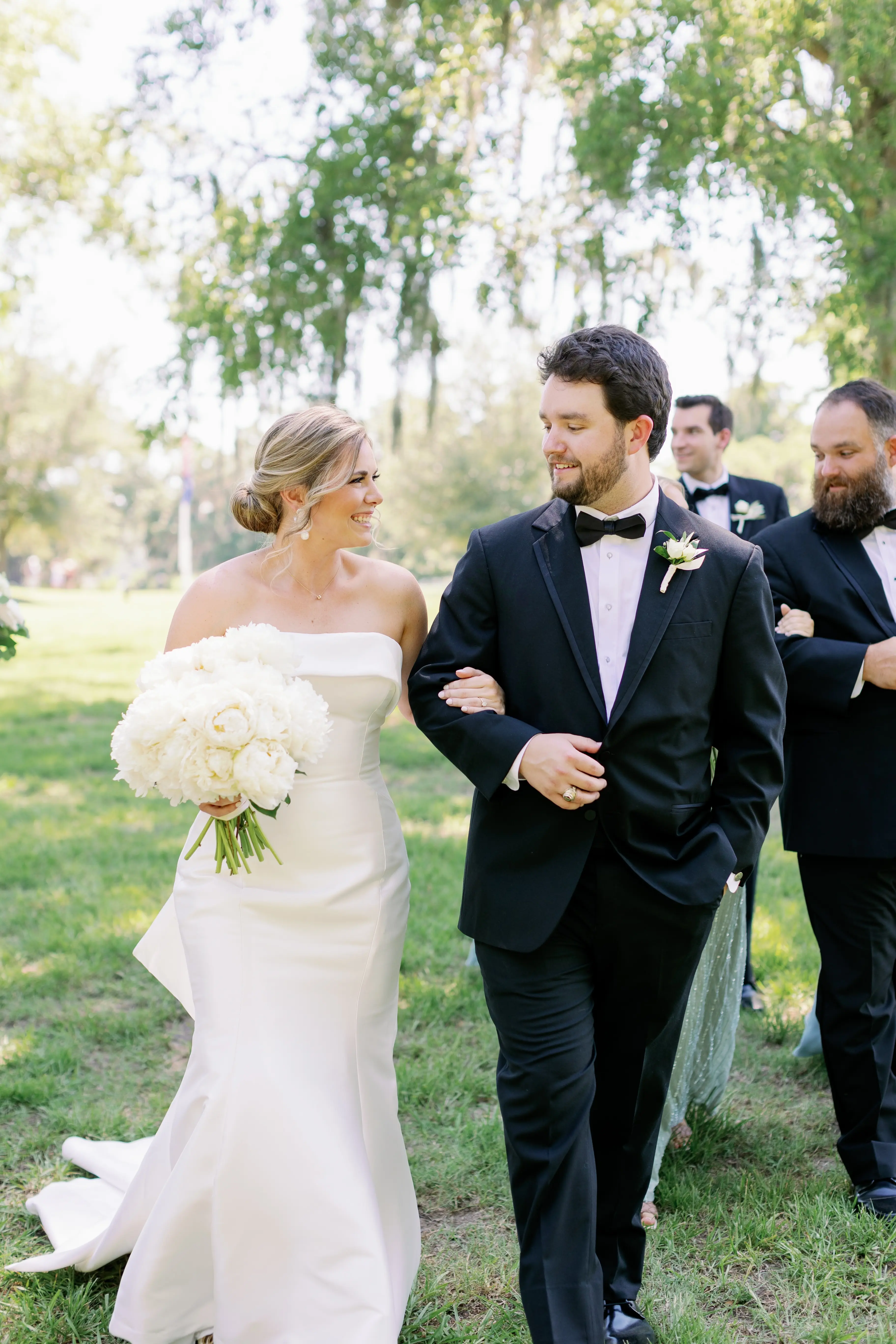 Bride with groom wearing strapless elegant mermaid wedding dress outdoors holding flower bouquet.