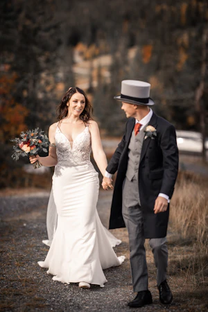 Bride wearing wedding dress called Nikki holding hands with her groom in a top hat.