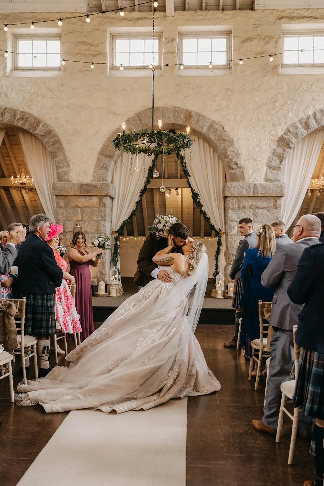 Bride wearing Norvinia by Sottero and Midgley kissing her husband as they exit the ceremony