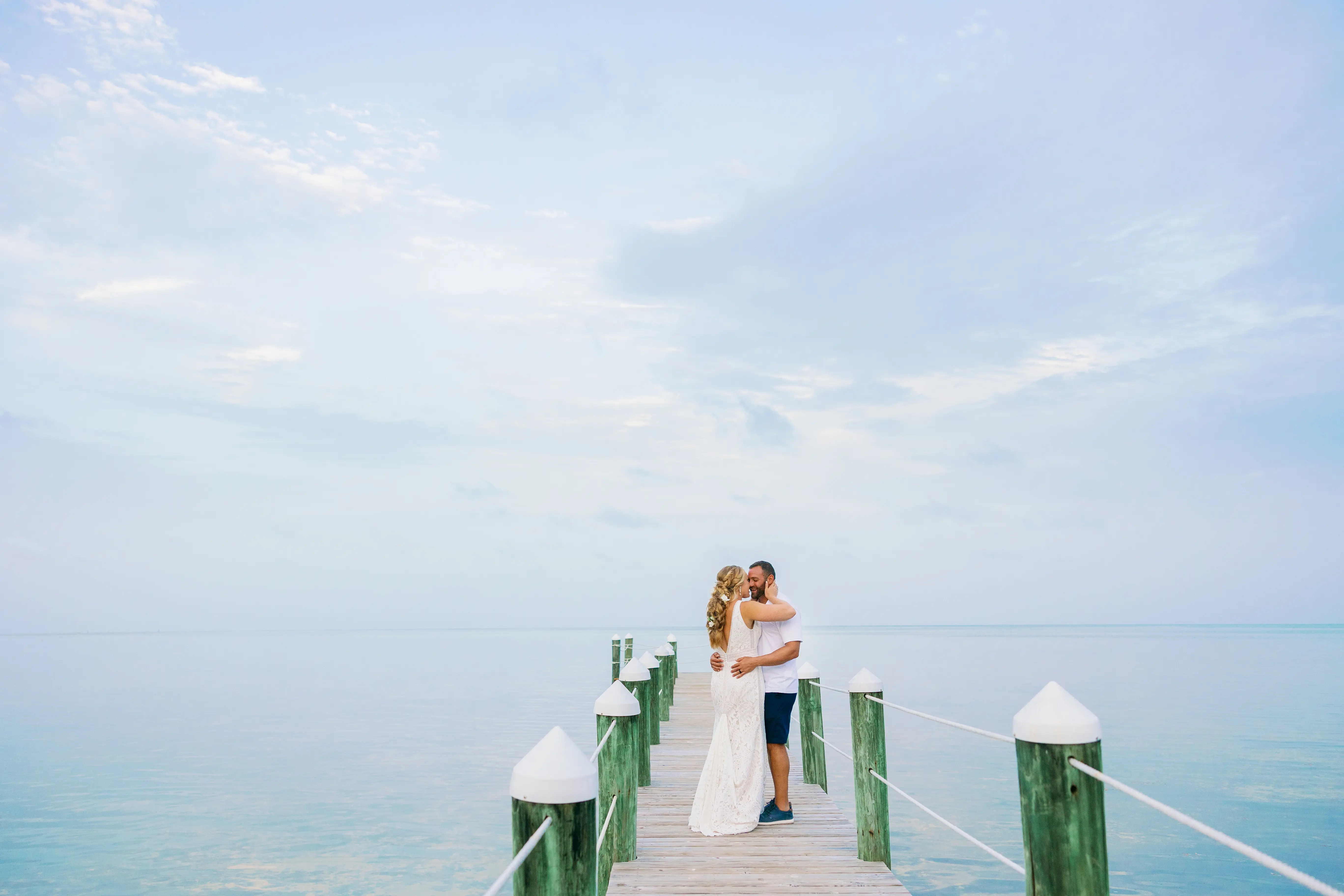 Newlyweds stood on a pier hugging and looking into each others eyes.