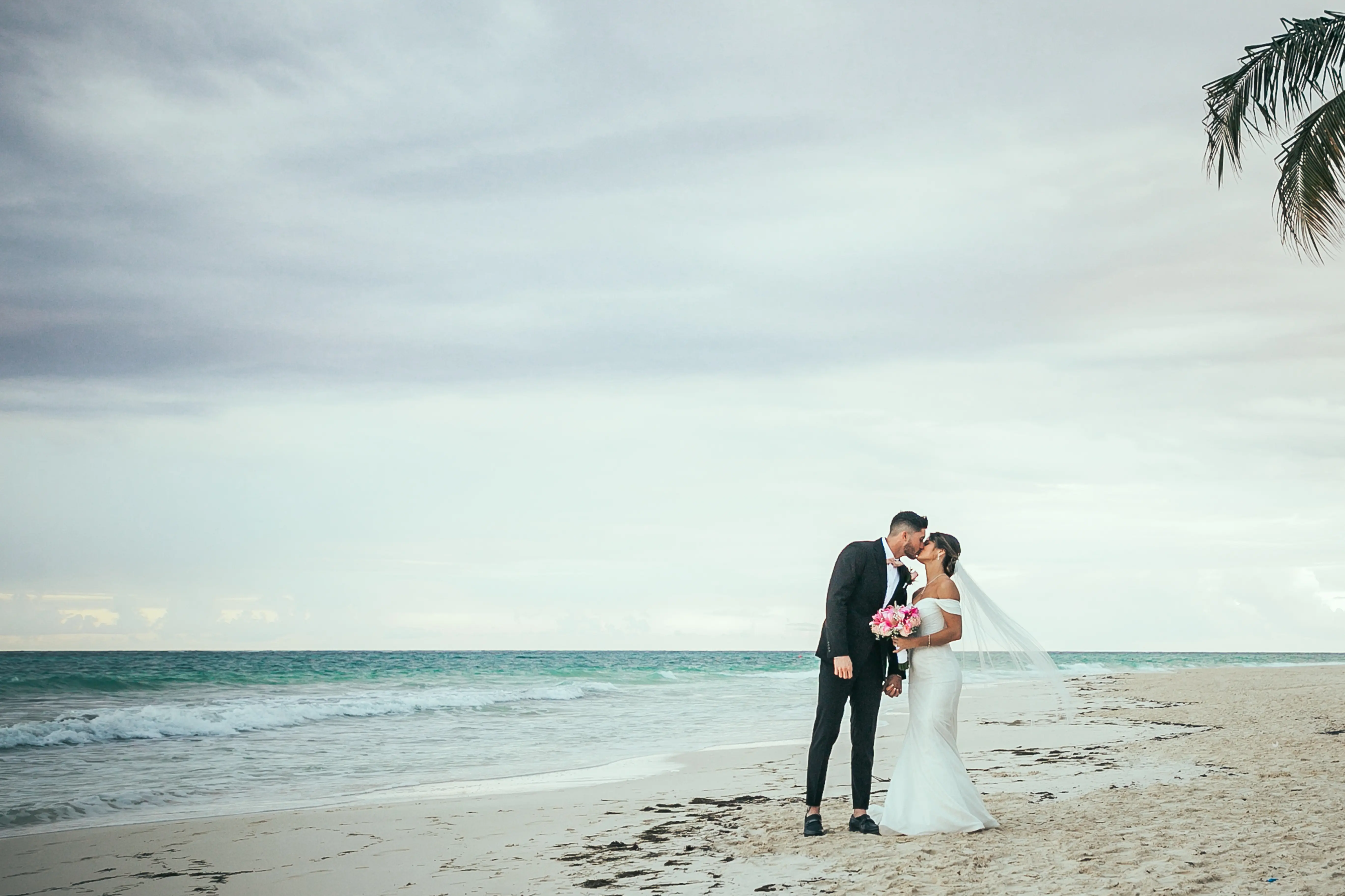 Bride Wearing Sparkly Fit And Flare Wedding Dress Called Anniston Lane By Maggie Sottero Kissing Groom On The Beach