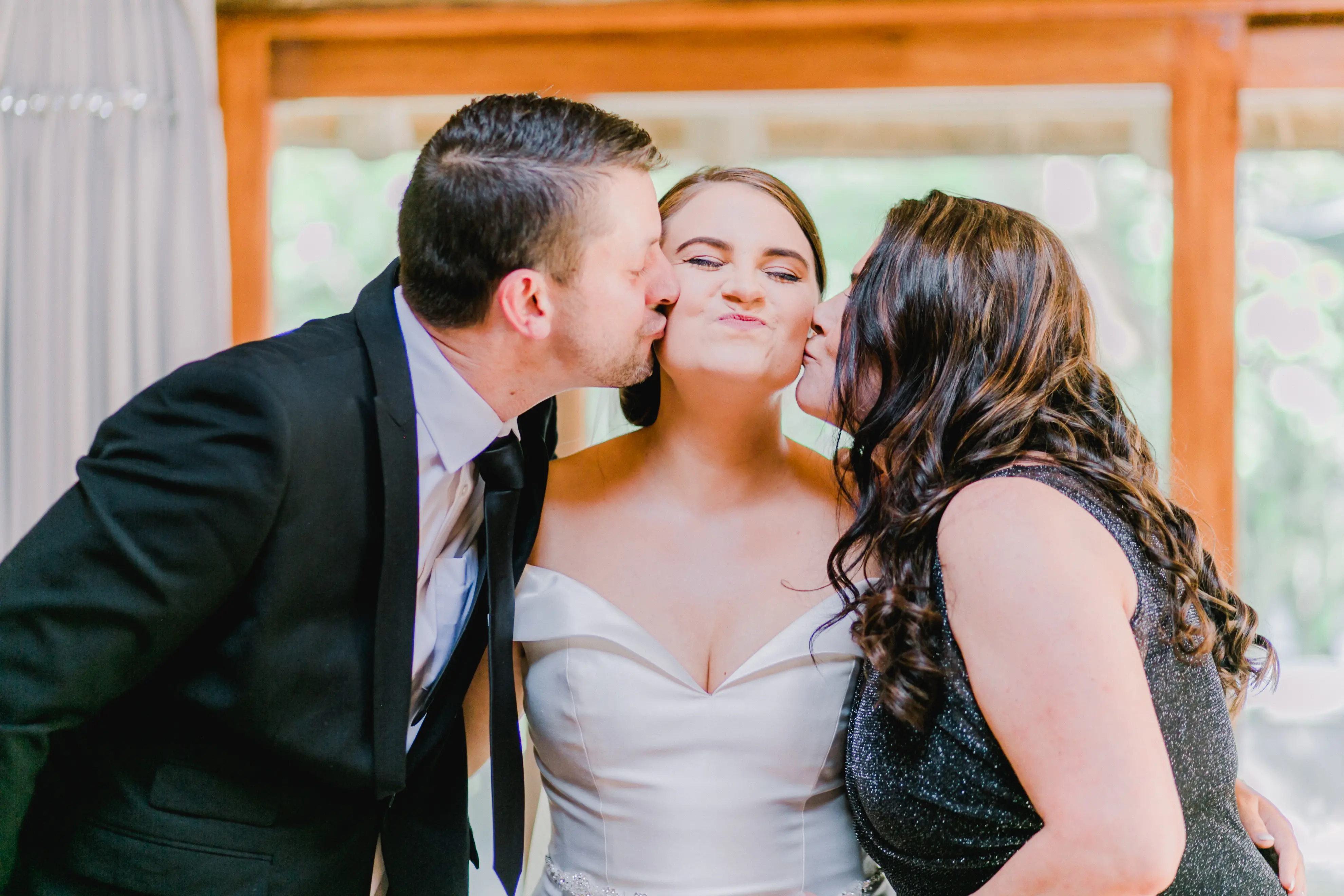 Bride Wearing Off-The-Shoulder A-Line Wedding Dress Called Coral By Rebecca Ingram Getting Kissed By Family
