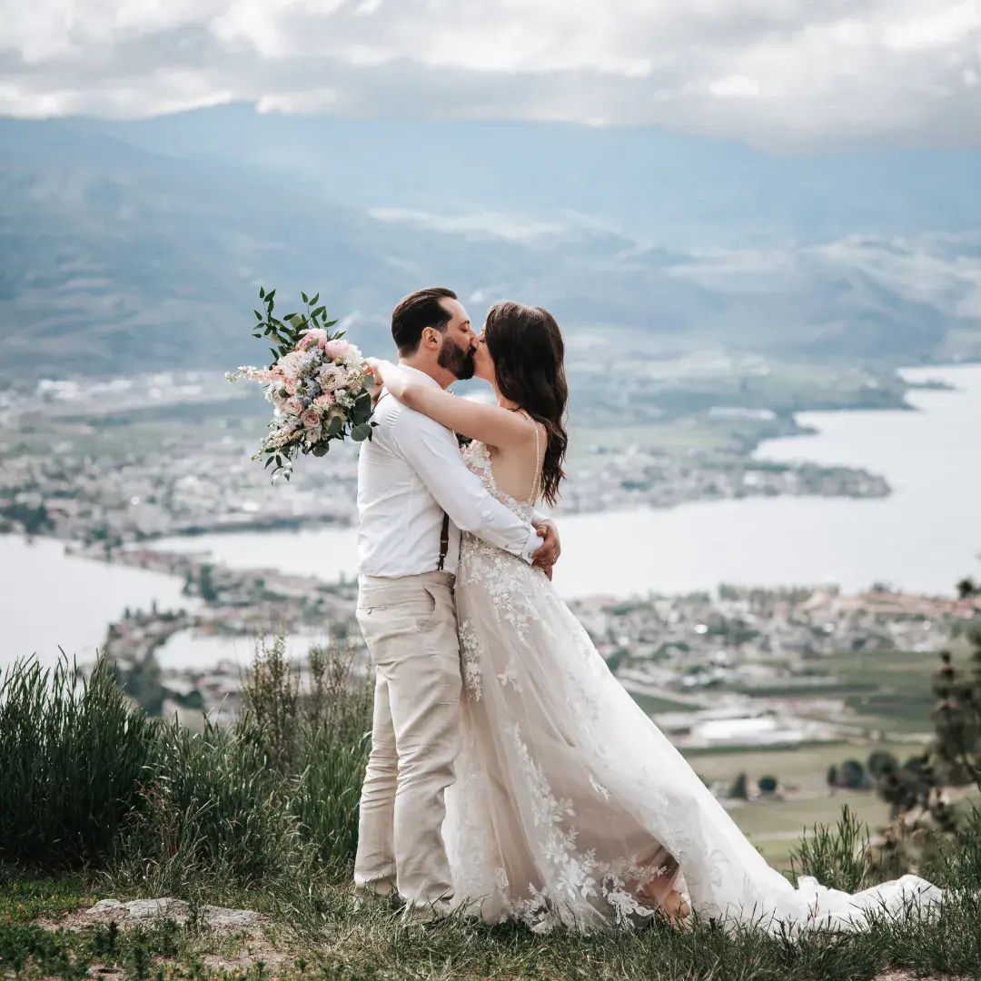 Bride Wearing Romantic Key Hole Back A-Line Wedding Dress Called Marlow By Maggie Sottero Kissing Groom Holding Flower Bouquet