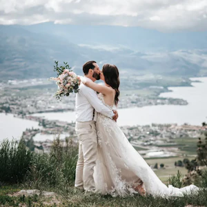 Bride Wearing Romantic Key Hole Back A-Line Wedding Dress Called Marlow By Maggie Sottero Kissing Groom Holding Flower Bouquet