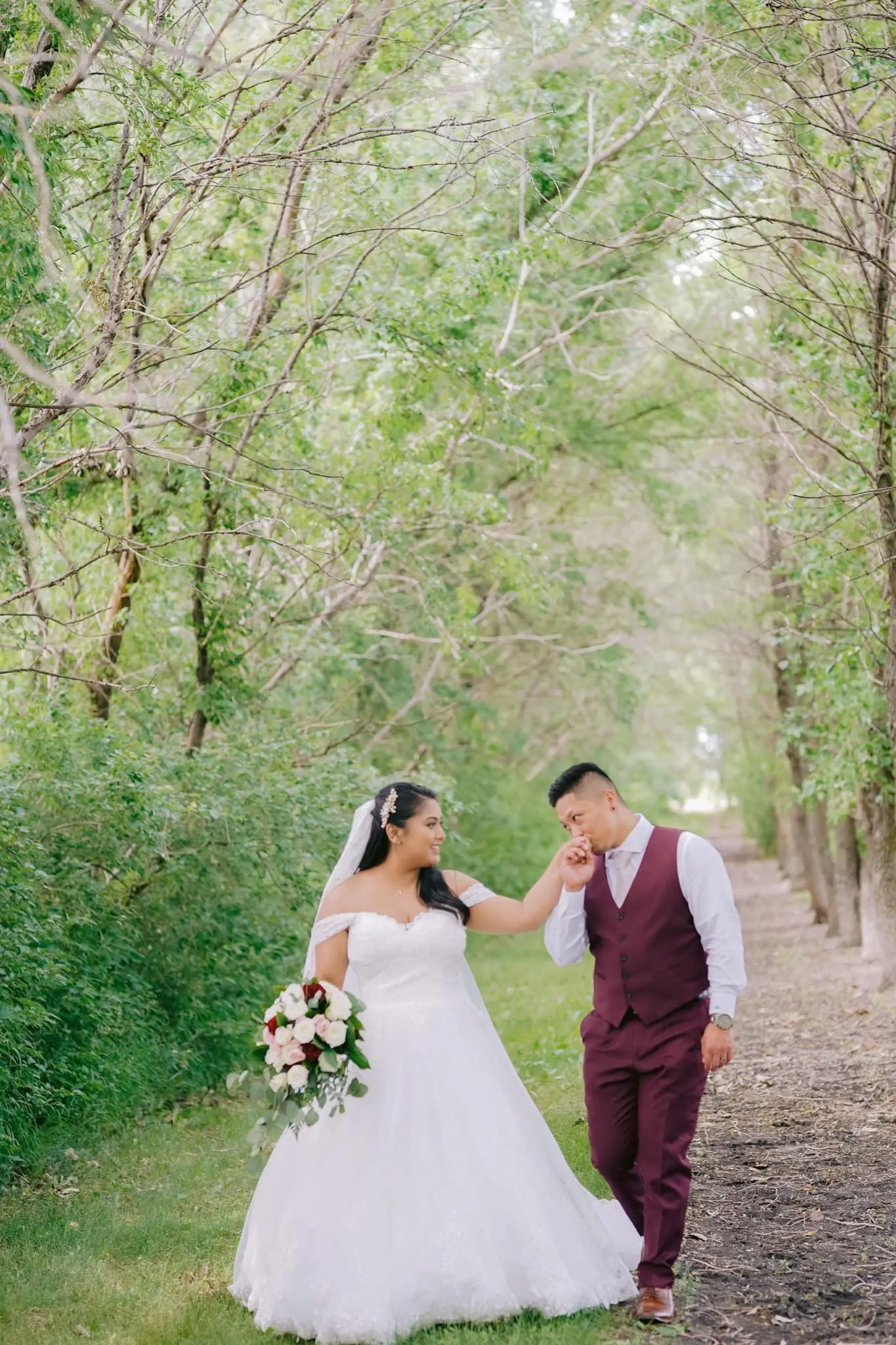 Groom kissing bride's hand while walking a path in the woods.