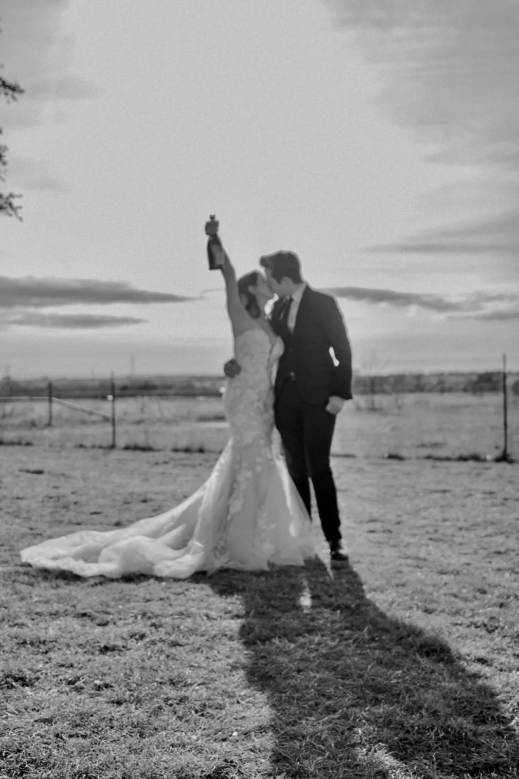 Bride wearing Bridget by Maggie Sottero kissing her husband and holding up a bottle