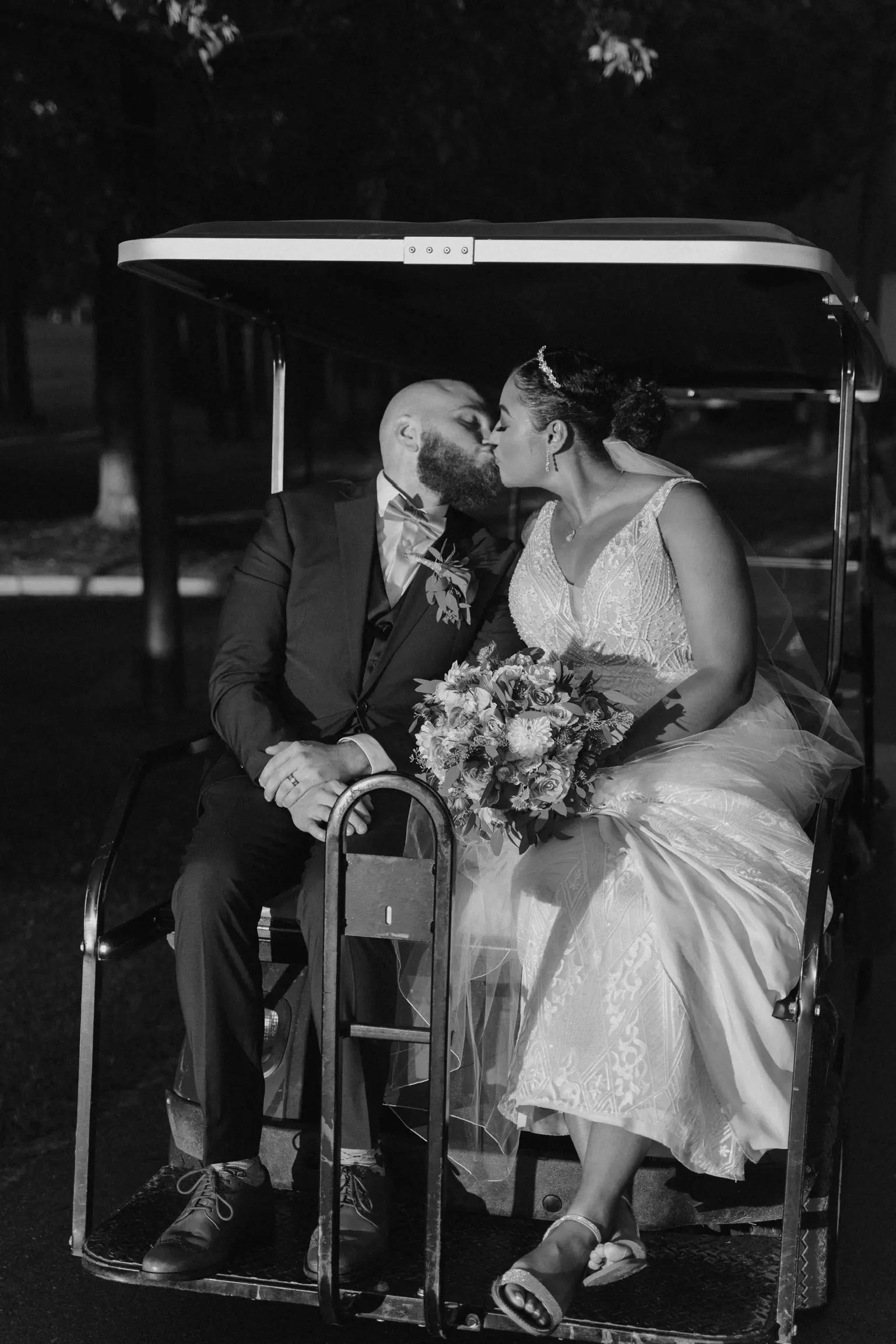 Bride kissing groom on golf cart wearing art deco-inspired beaded wedding dress.