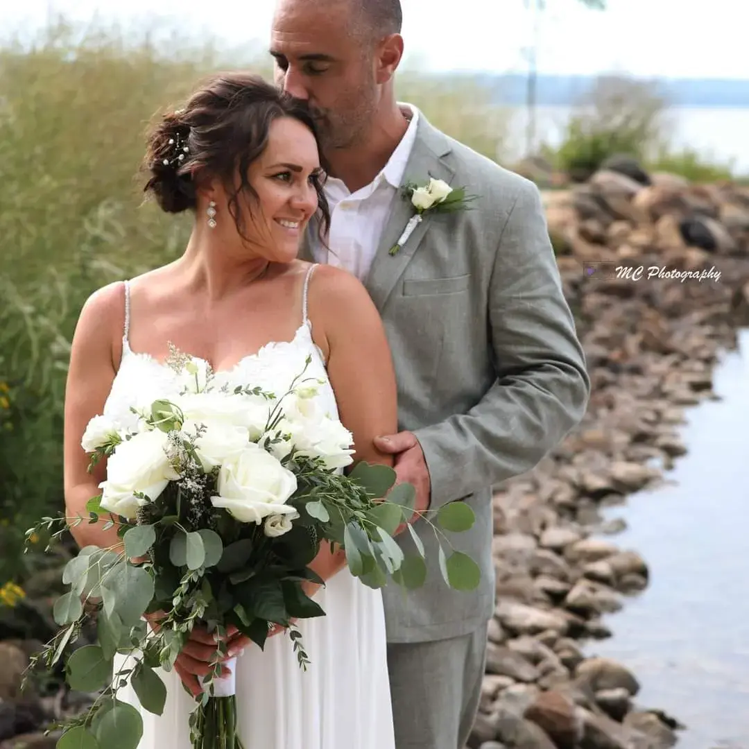 Bride Wearing Simple Chiffon Wedding Dress Called Marta Lynette By Rebecca Ingram Holding Bouquet With Groom On Rocky Beach