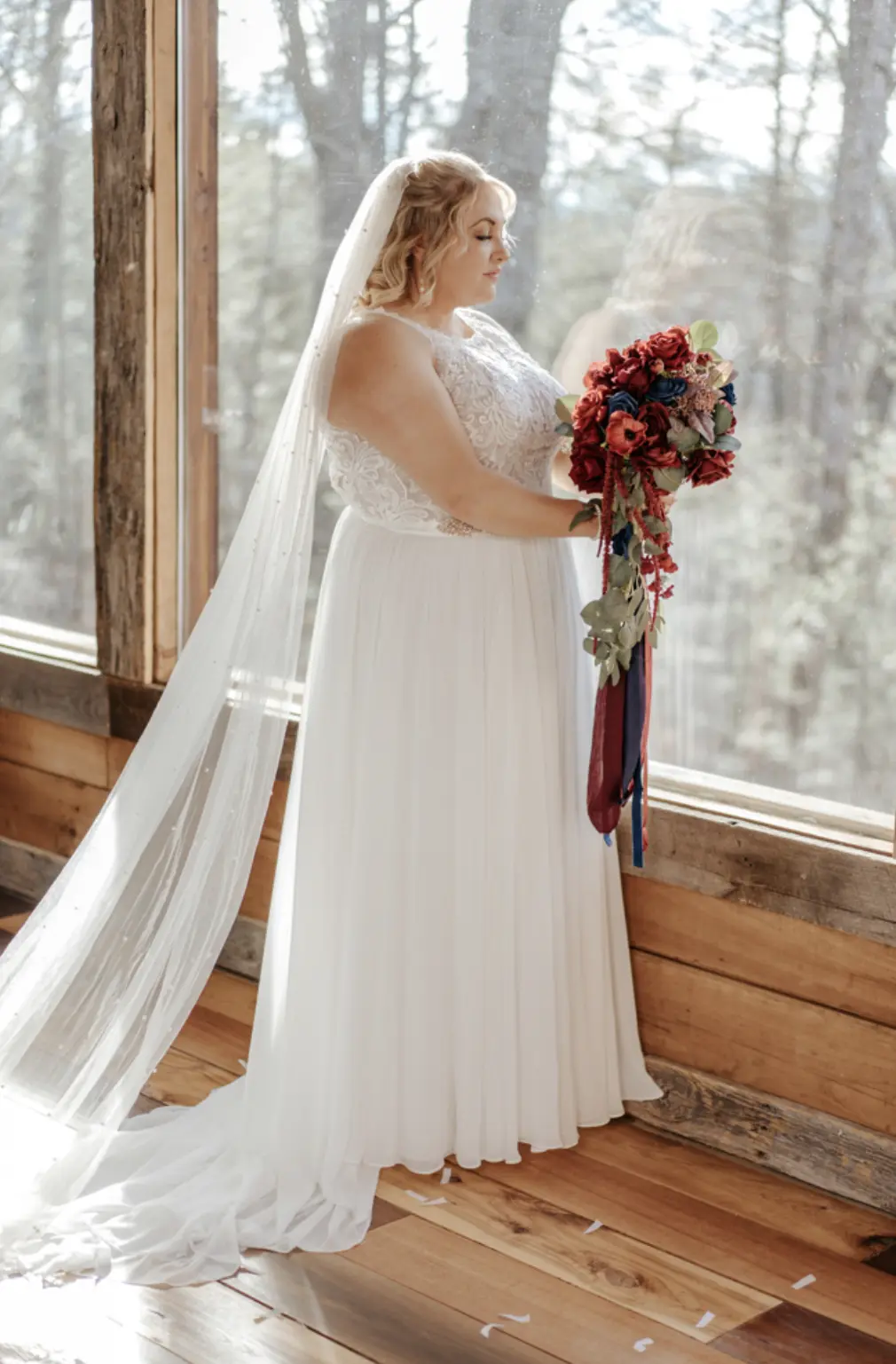 Bride In Chiffon Wedding Dress Called Tasha By Rebecca Ingram With Red And Blue Rose Bouquet