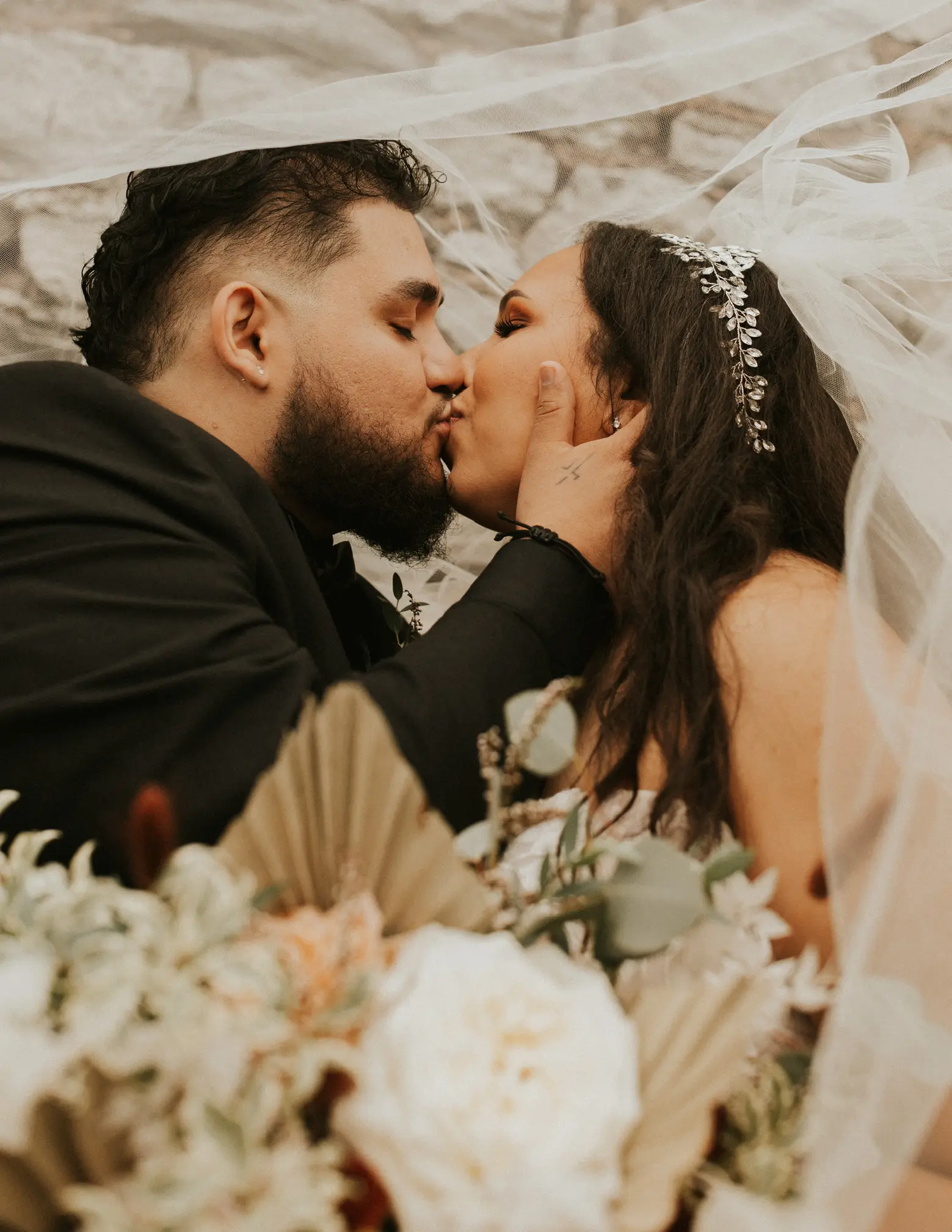 Bride Kissing Groom Under Wedding Veil Holding Flower Bouquet
