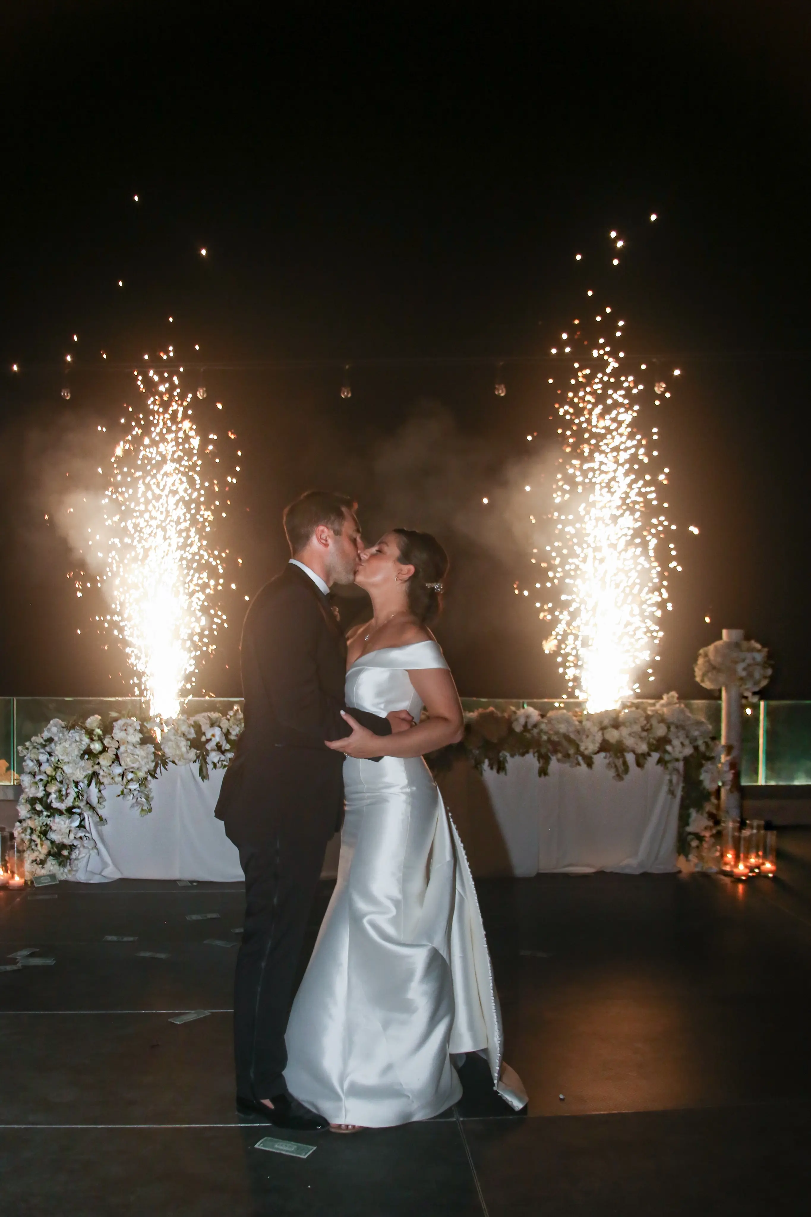 Bride wearing Simple Fit-and-Flare Wedding Dress called Josie by Rebecca Ingram kissing the groom with sparklers behind them