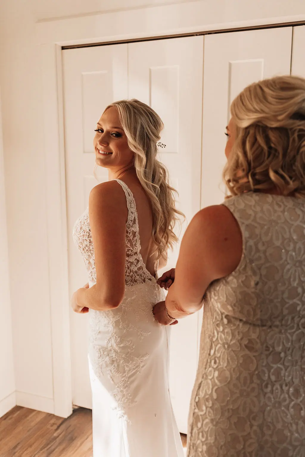 Mother of bride fastening the wedding dress called Carmen.