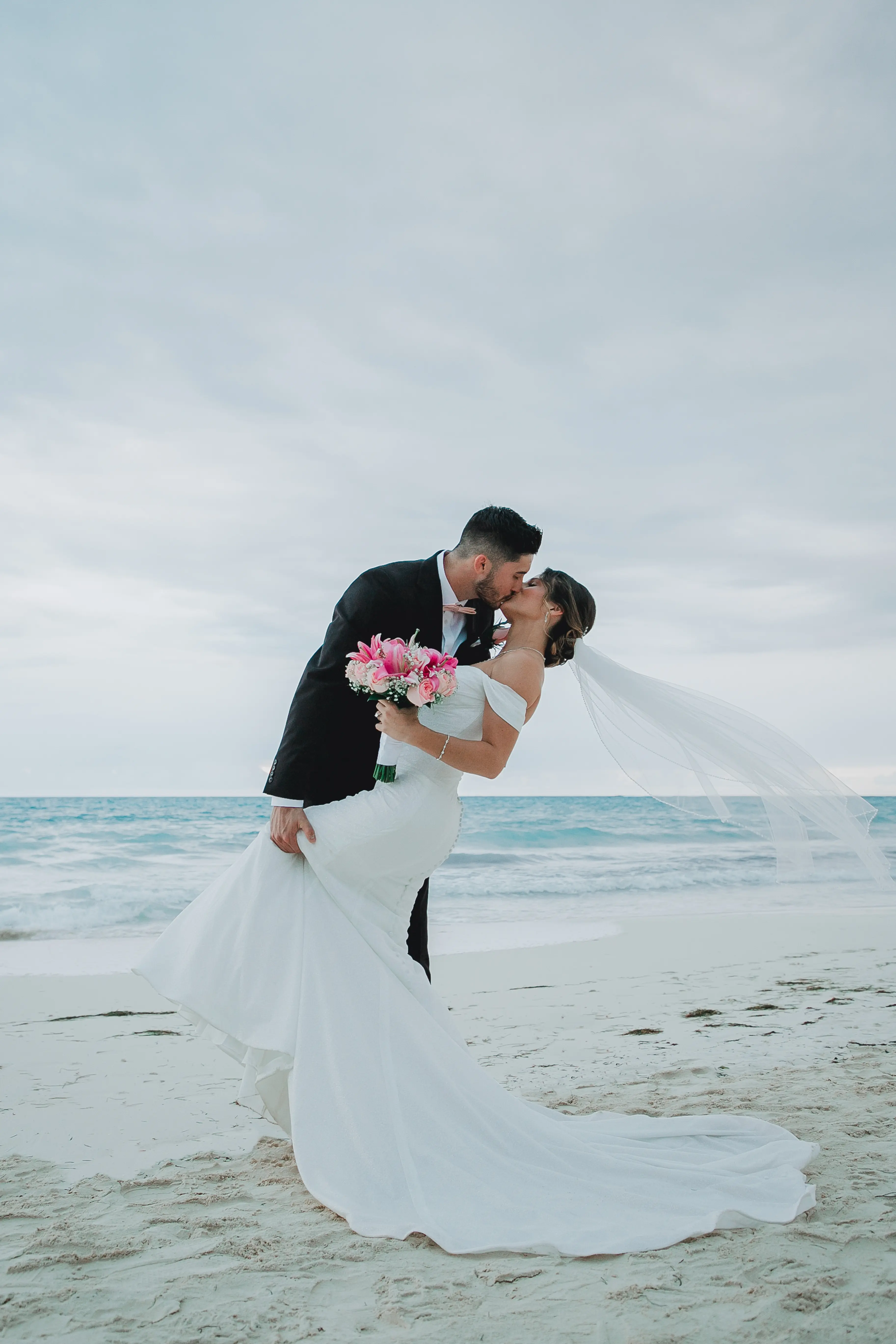 Bride Wearing Sparkly Fit And Flare Wedding Dress Called Anniston Lane By Maggie Sottero Kissing Groom On The Beach