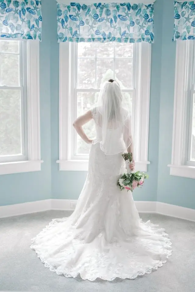 Bride Standing by Window Wearing a Classic Lace Wedding Dress Called Brenda by Rebecca Ingram
