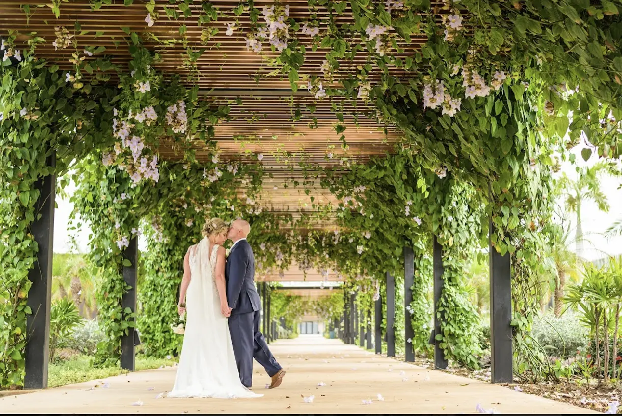 Bride and groom holding hands as he kisses her forehead.
