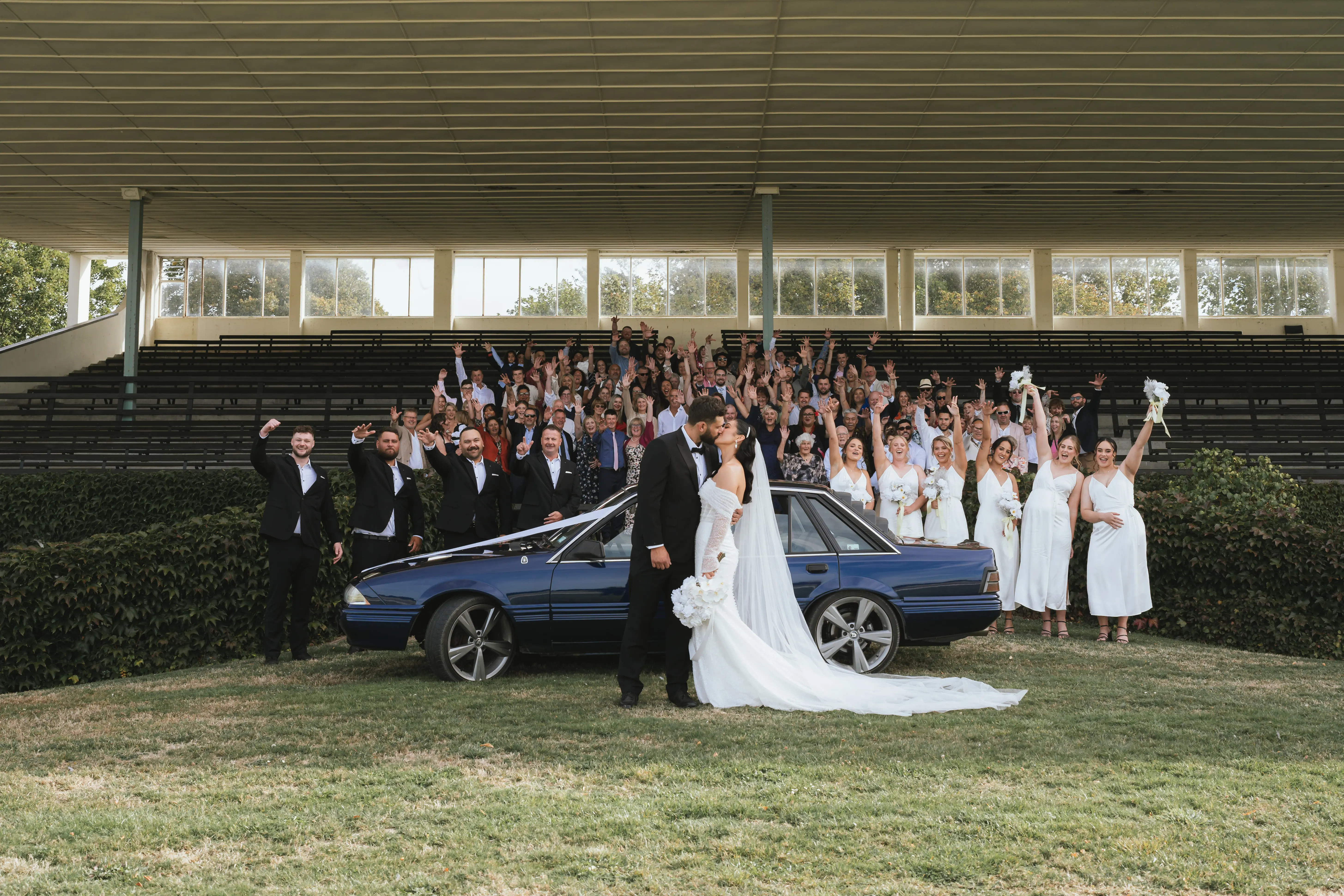 Bride wearing Drew by Maggie Sottero kissing her husband in front of a car and guests