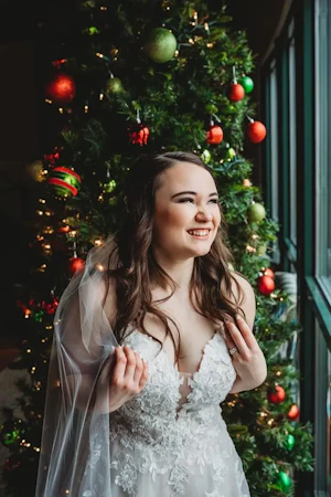 Bride Standing In Front Of Christmas Tree. Bride Wearing Lace Sparkly Wedding Dress Called Stevie By Maggie Sottero