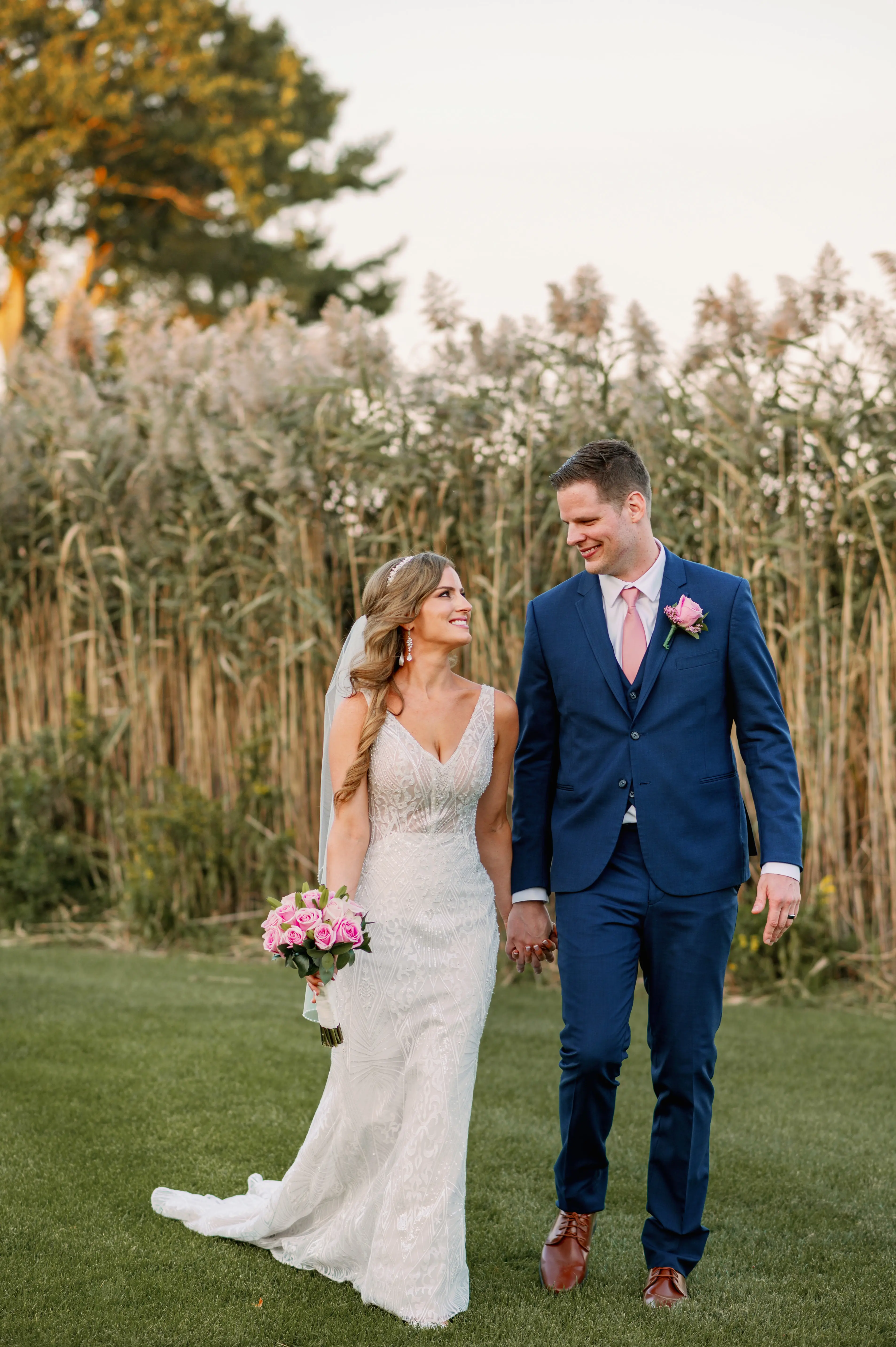 bride and groom holding hands in front of tall grass.