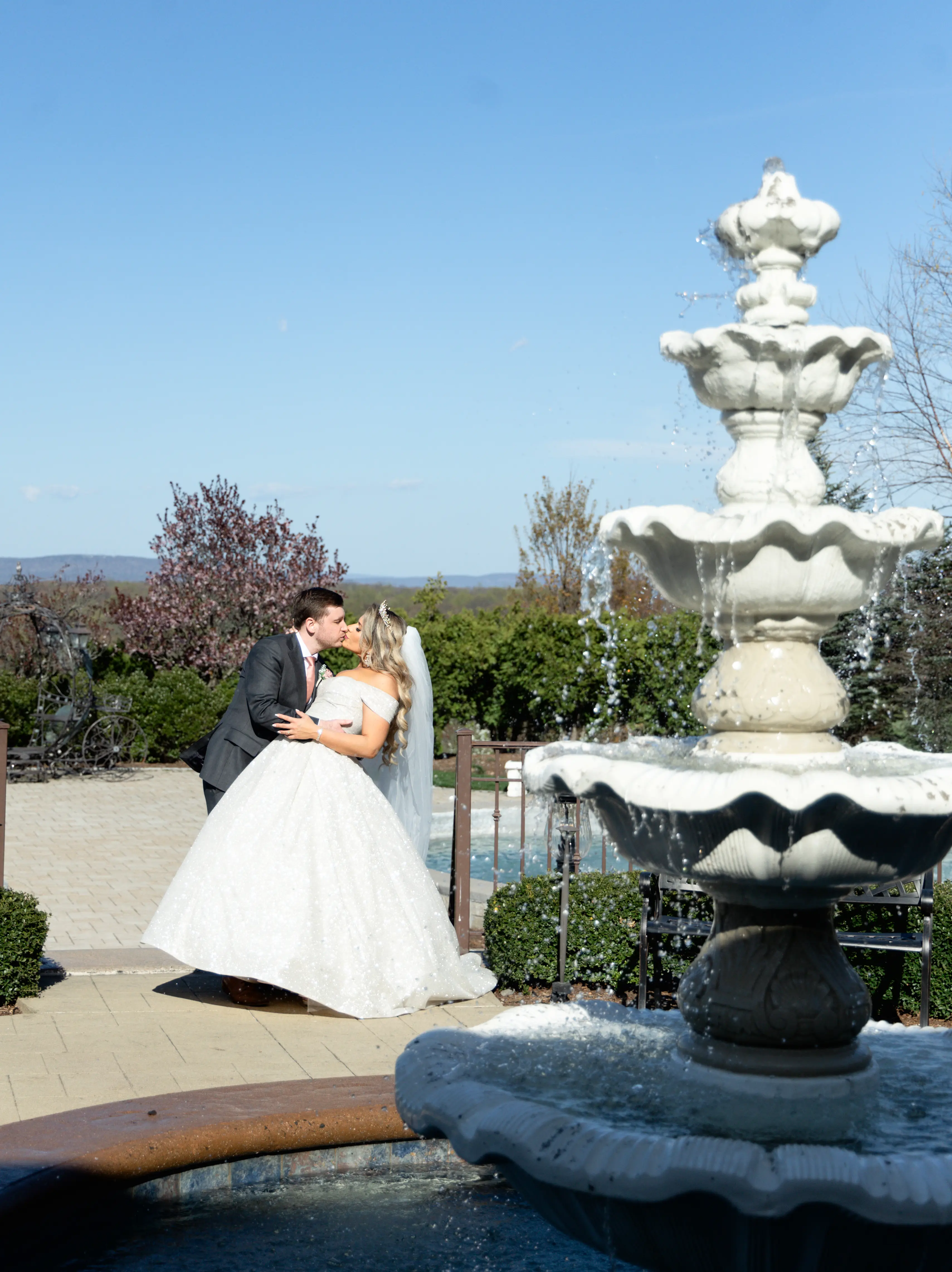 Bride wearing Anniston by Maggie Sottero kissing her husband by a fountain