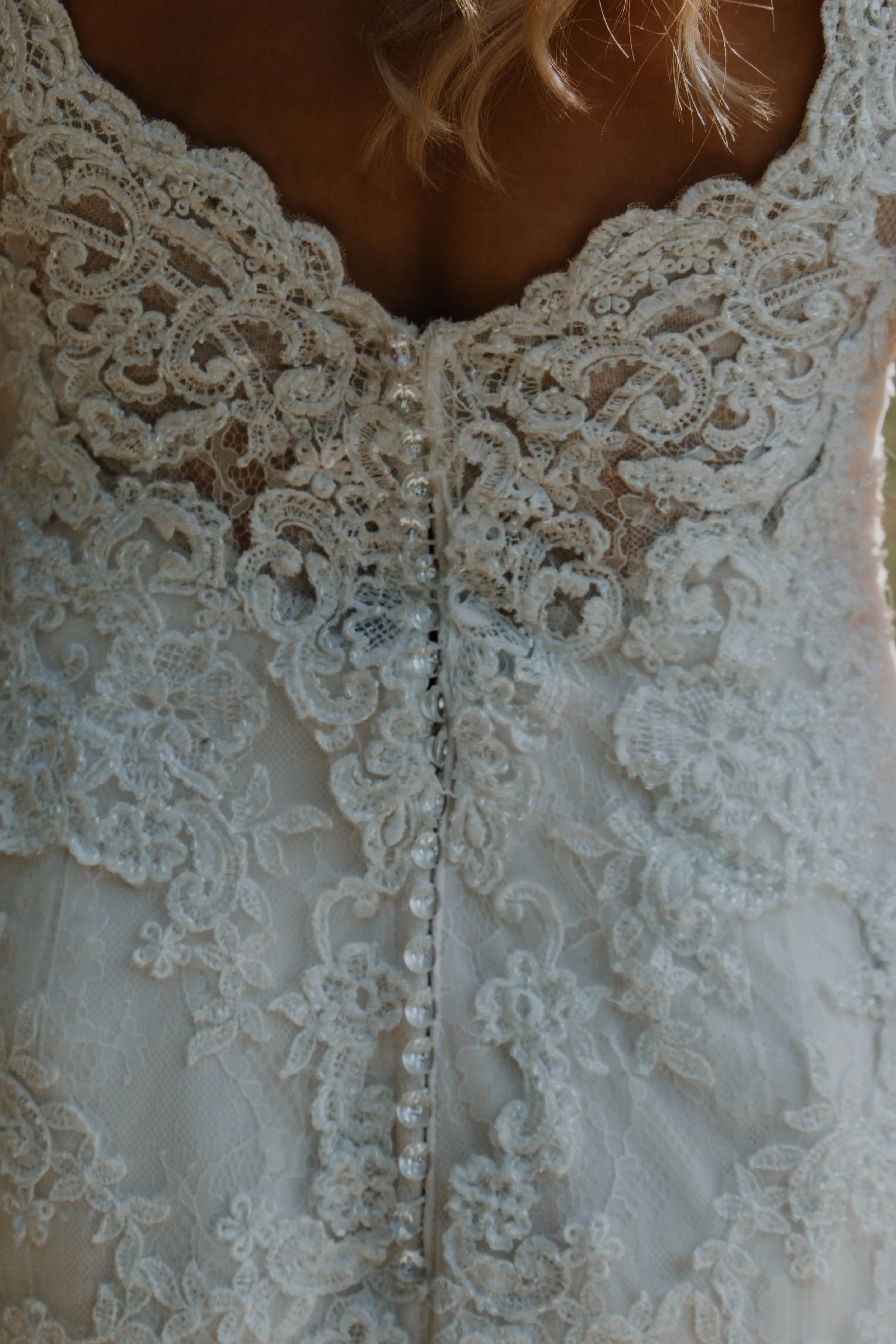 detail of lace wedding dress and clear buttons.