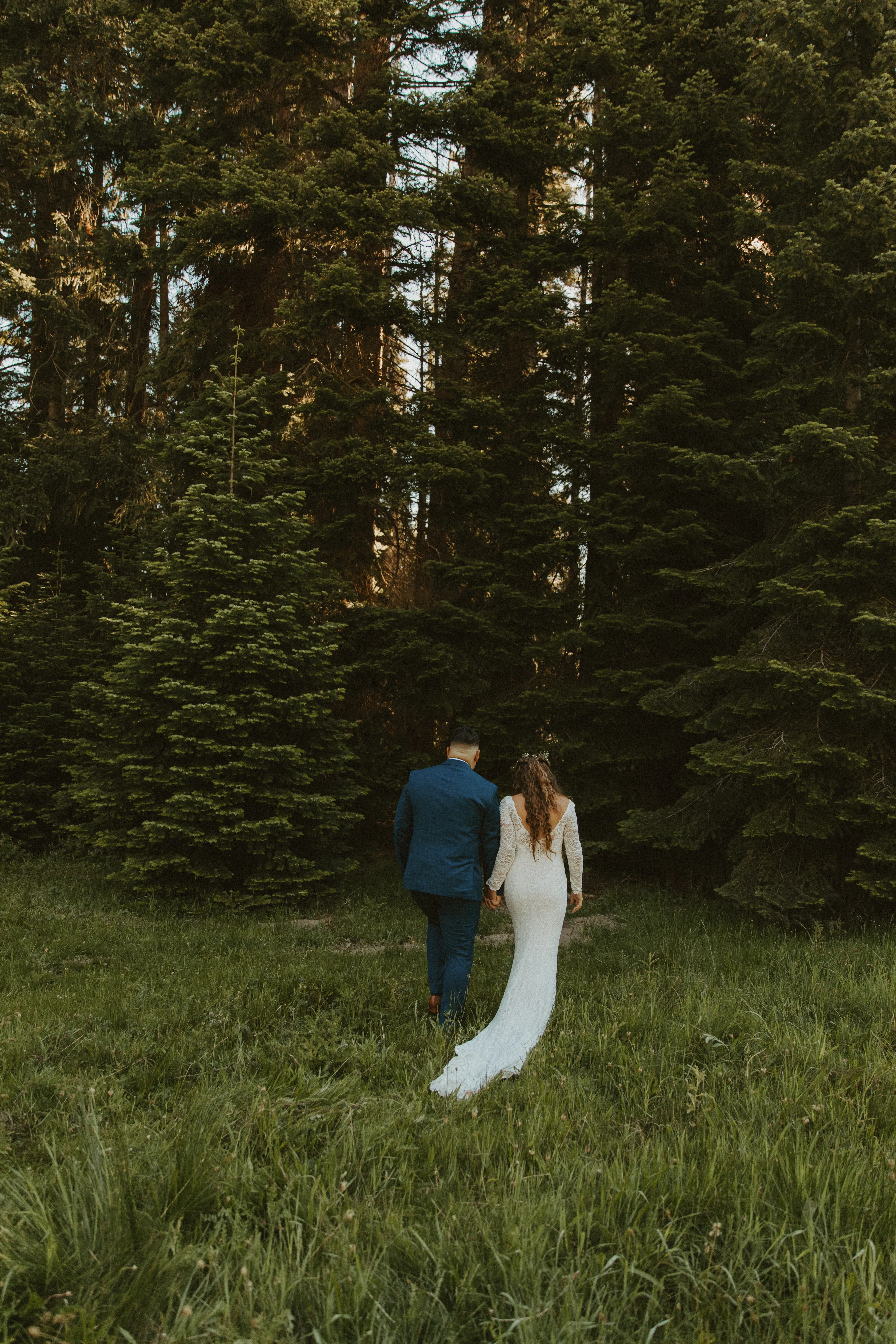 Newlyweds walking towards the woods together.