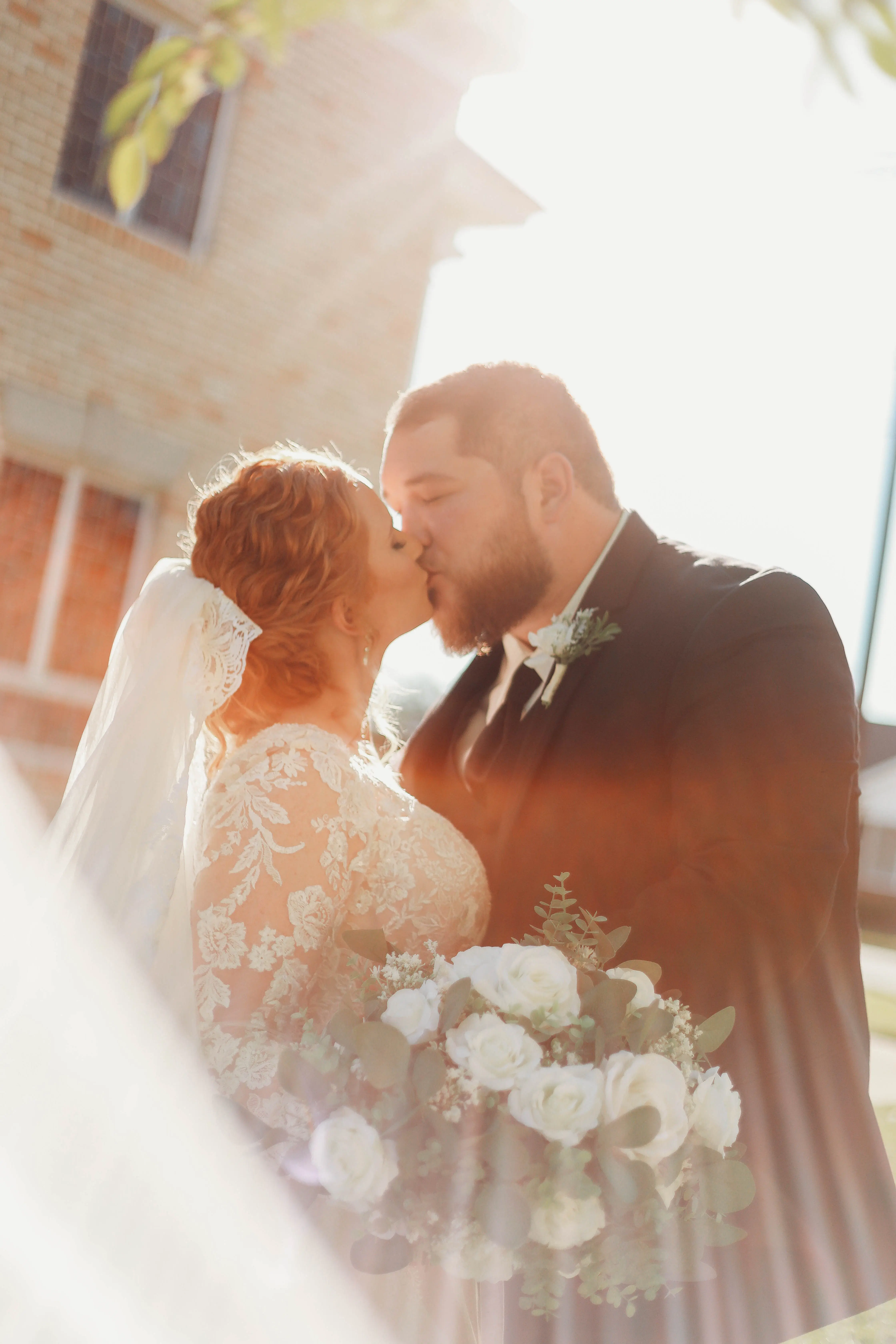Bride Wearing Lace Long-Sleeve Wedding Gown Called Raphael By Maggie Sottero Kissing Groom