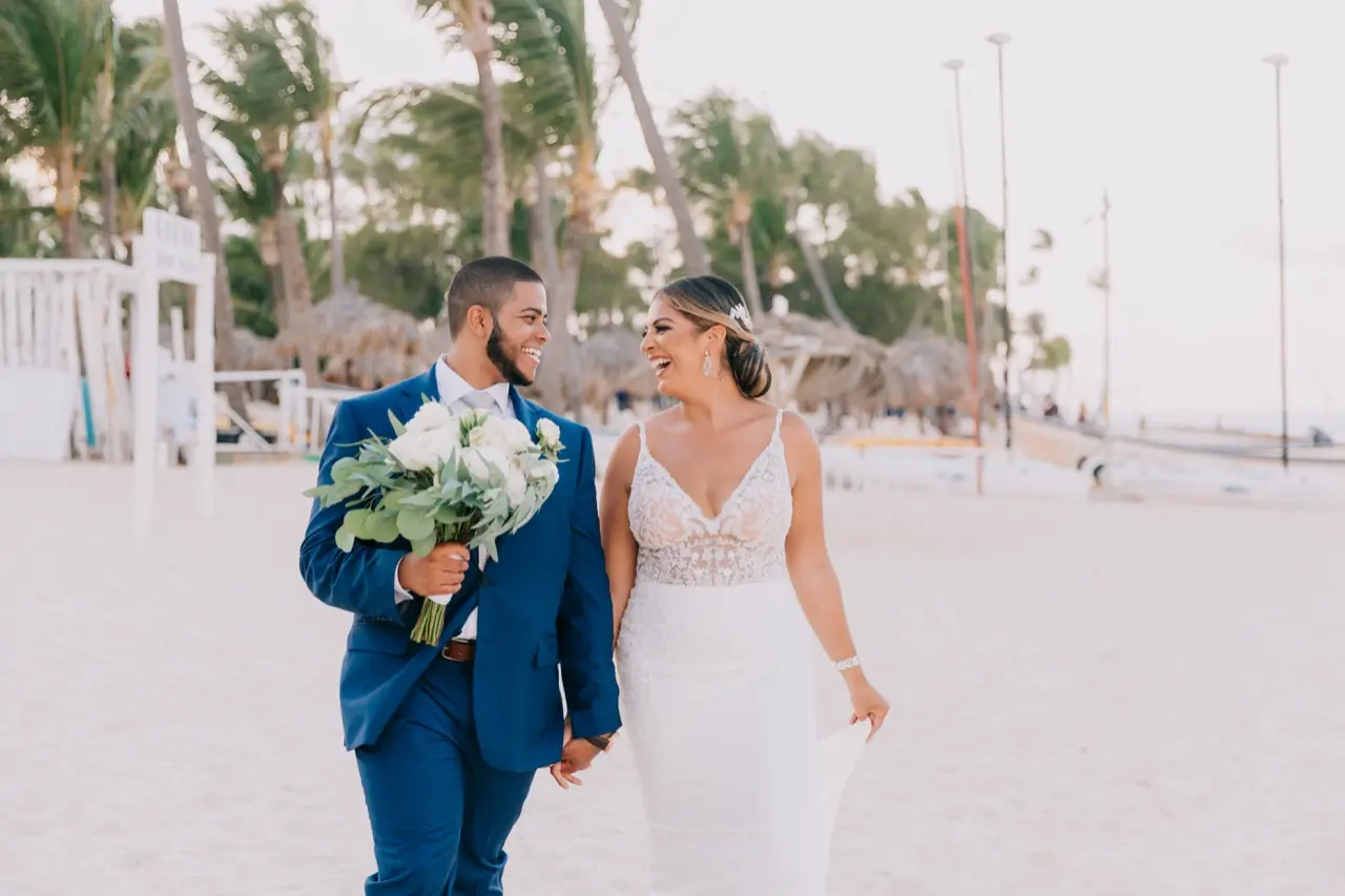 Groom holding bride ivory bouquet while walking and laughing on the beach.
