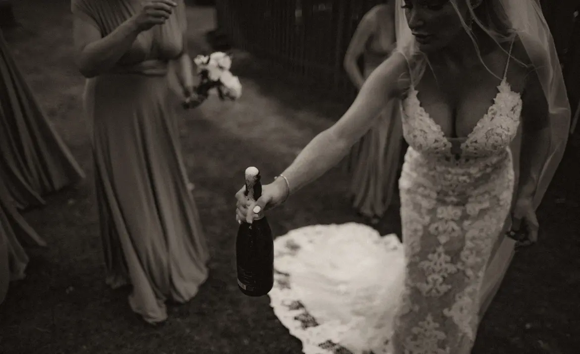 Bride wearing Lace Fit-and-Flare Wedding Dress called Tuscany Lynette by Maggie Sottero holding champagne