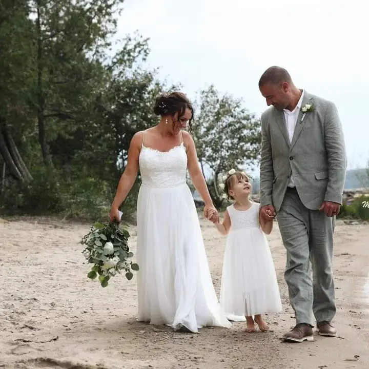 Bride Wearing Simple Chiffon Wedding Dress Called Marta Lynette By Rebecca Ingram Walking With Groom And Flower Girl On Beach