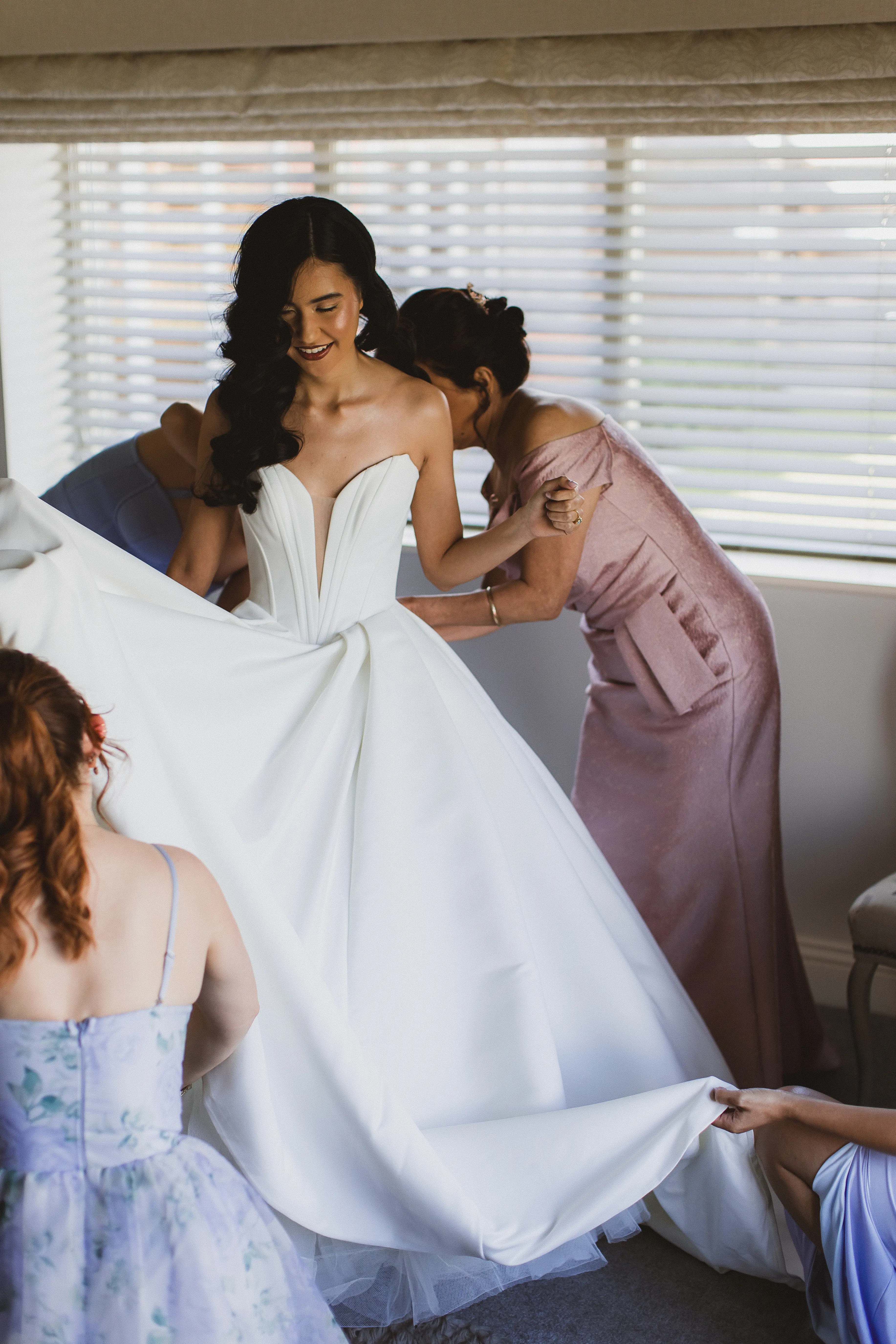 Bride wearing Derrick by Maggie Sottero being zipped up by her bridesmaids