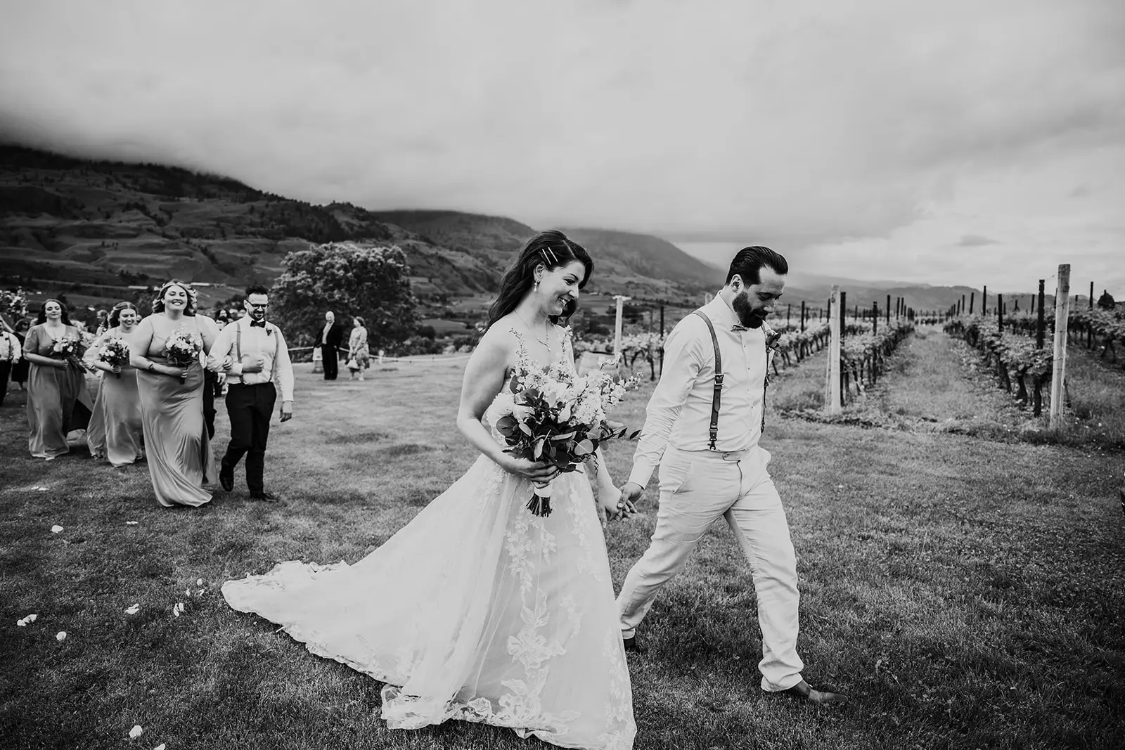 Bride Wearing Romantic Key Hole Back A-Line Wedding Dress Called Marlow By Maggie Sottero Walks With Groom Followed By Attendants