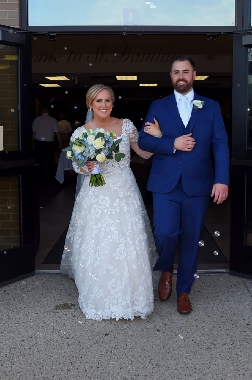 Bride Wearing Long Sleeve Floral Lace Wedding Dress Called Sawyer By Sottero and Midgley Walks Outside With Groom And Bubbles
