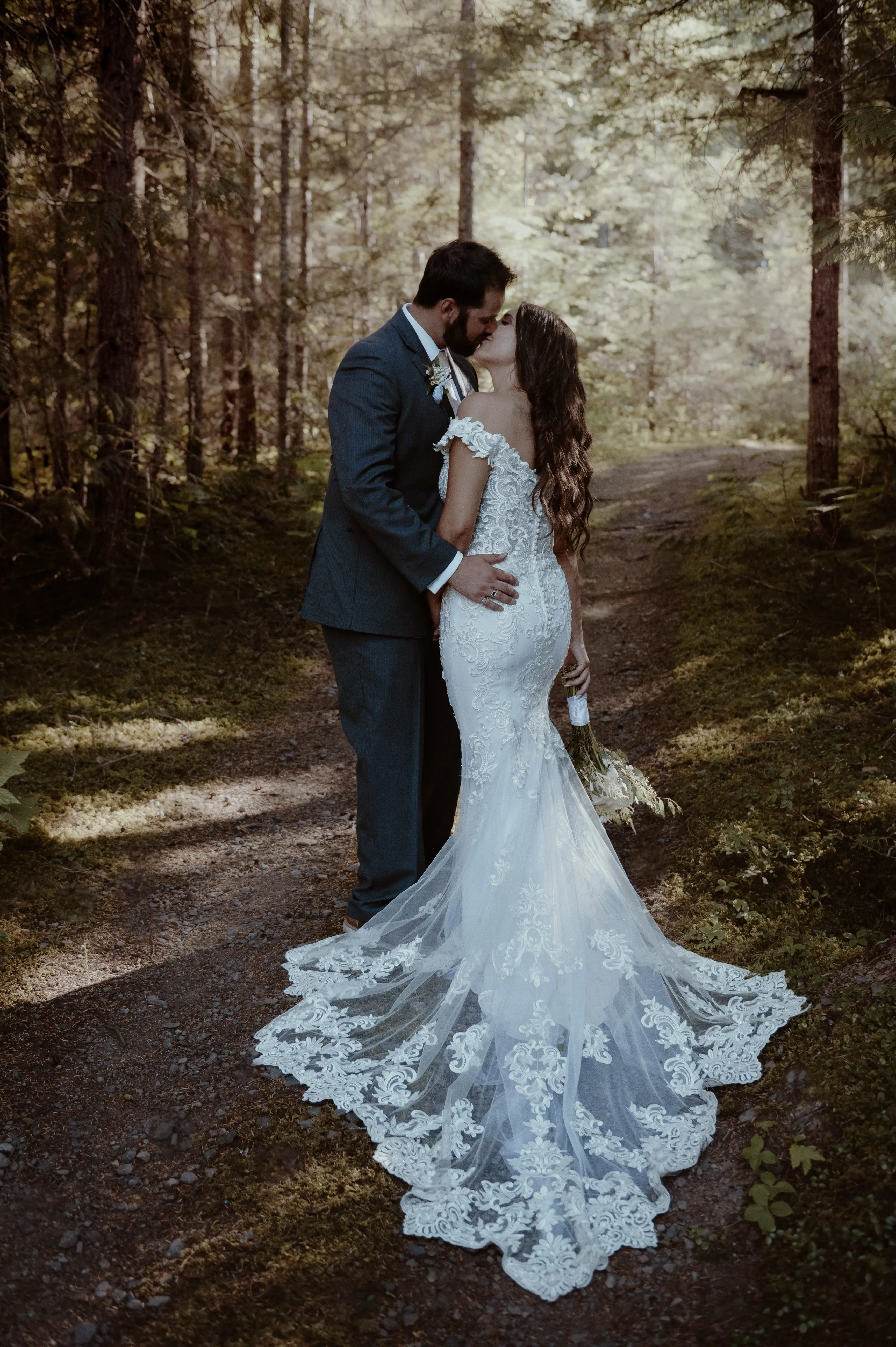 Bride with groom wearing romantic lace off-the-shoulder wedding dress outside in the mountains.