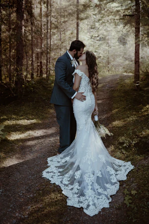 Bride with groom wearing romantic lace off-the-shoulder wedding dress outside in the mountains.