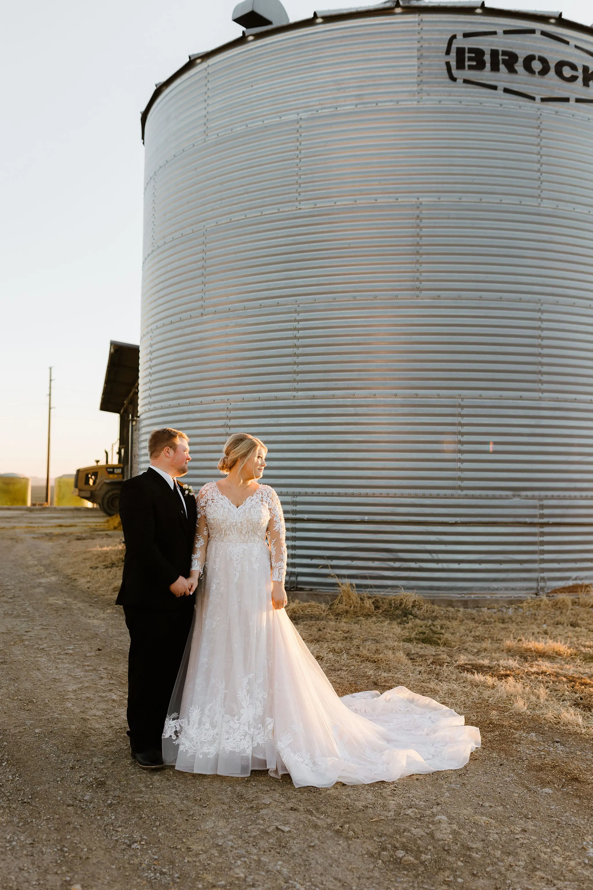 Bride And Groom Standing Together. Bride Wearing Layered Ball Gown Wedding Dress With Long Sleeves Called Zander By Sottero And Midgley