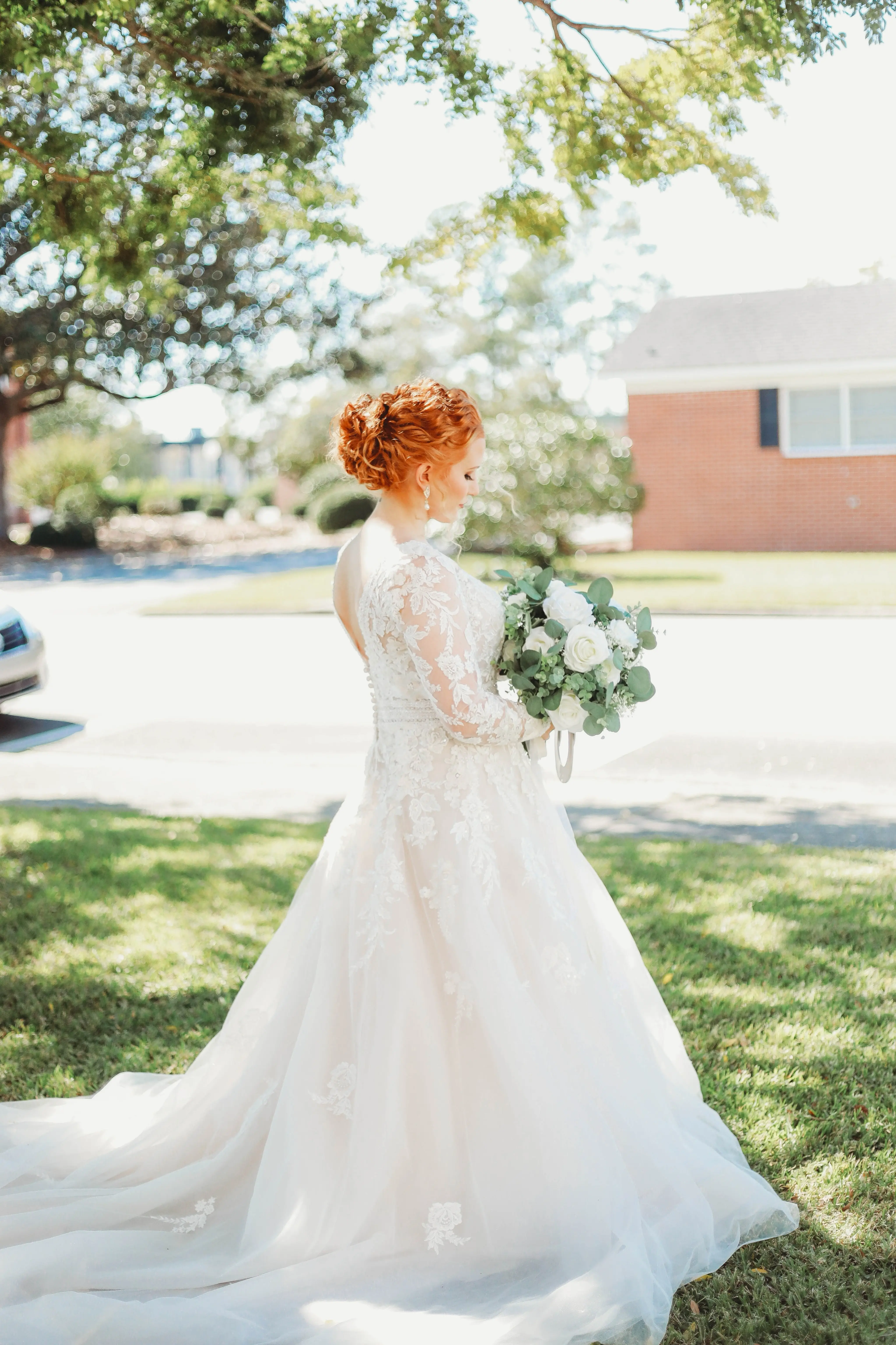 Bride Wearing Lace Long-Sleeve Wedding Gown Called Raphael By Maggie Sottero Holding White Rose Bouquet