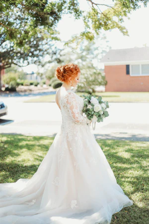 Bride Wearing Lace Long-Sleeve Wedding Gown Called Raphael By Maggie Sottero Holding White Rose Bouquet