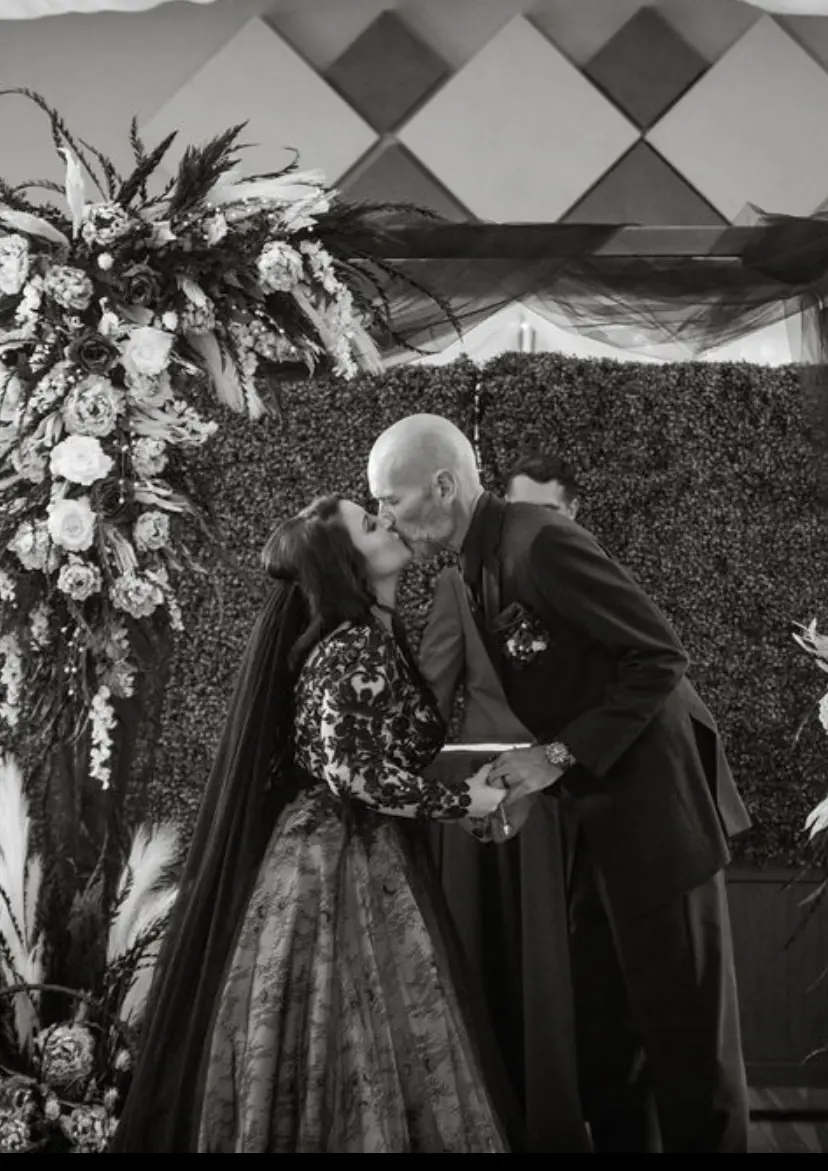 Bride And Groom Sharing Ceremony Kiss. Bride Wearing Black Lace Ballgown With Long Sleeves Called Zander By Sottero And Midgley